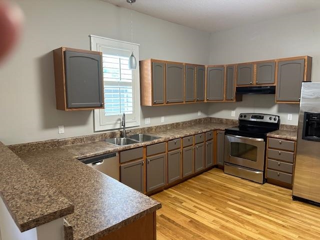 Kitchen with appliances with stainless steel finishes, light hardwood / wood-style flooring, kitchen peninsula, and sink