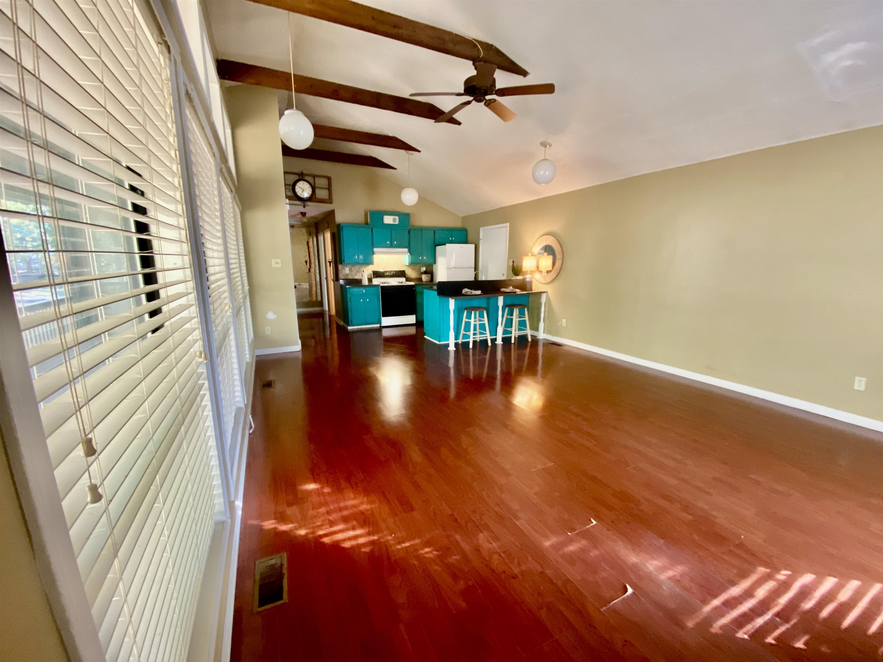 Greatroom features a wall of windows with lots of nature lighting,  ceiling fan, dark style flooring, along with a lofted ceiling with beams.