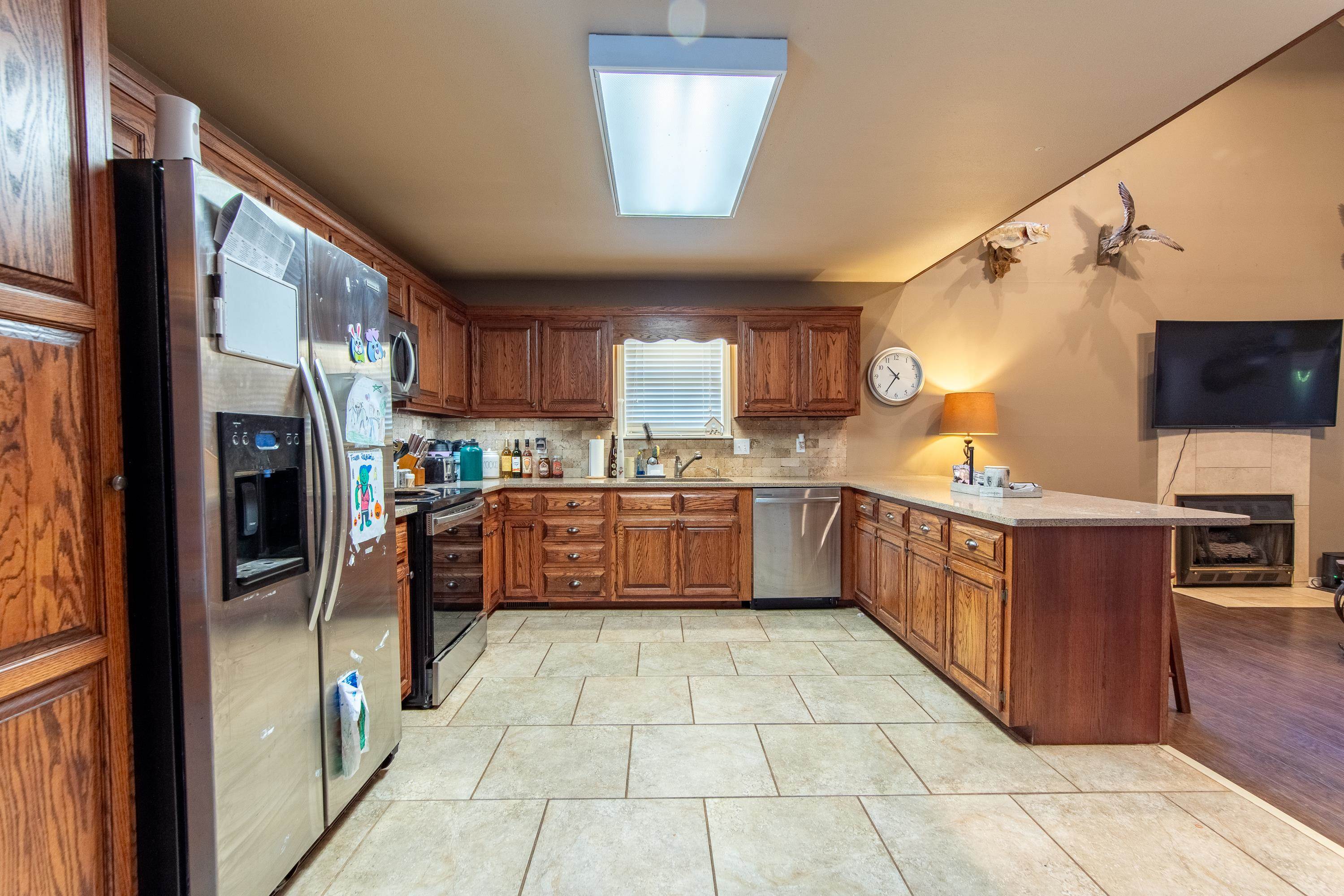 Kitchen featuring backsplash, light tile patterned floors, stainless steel appliances, kitchen peninsula, and sink