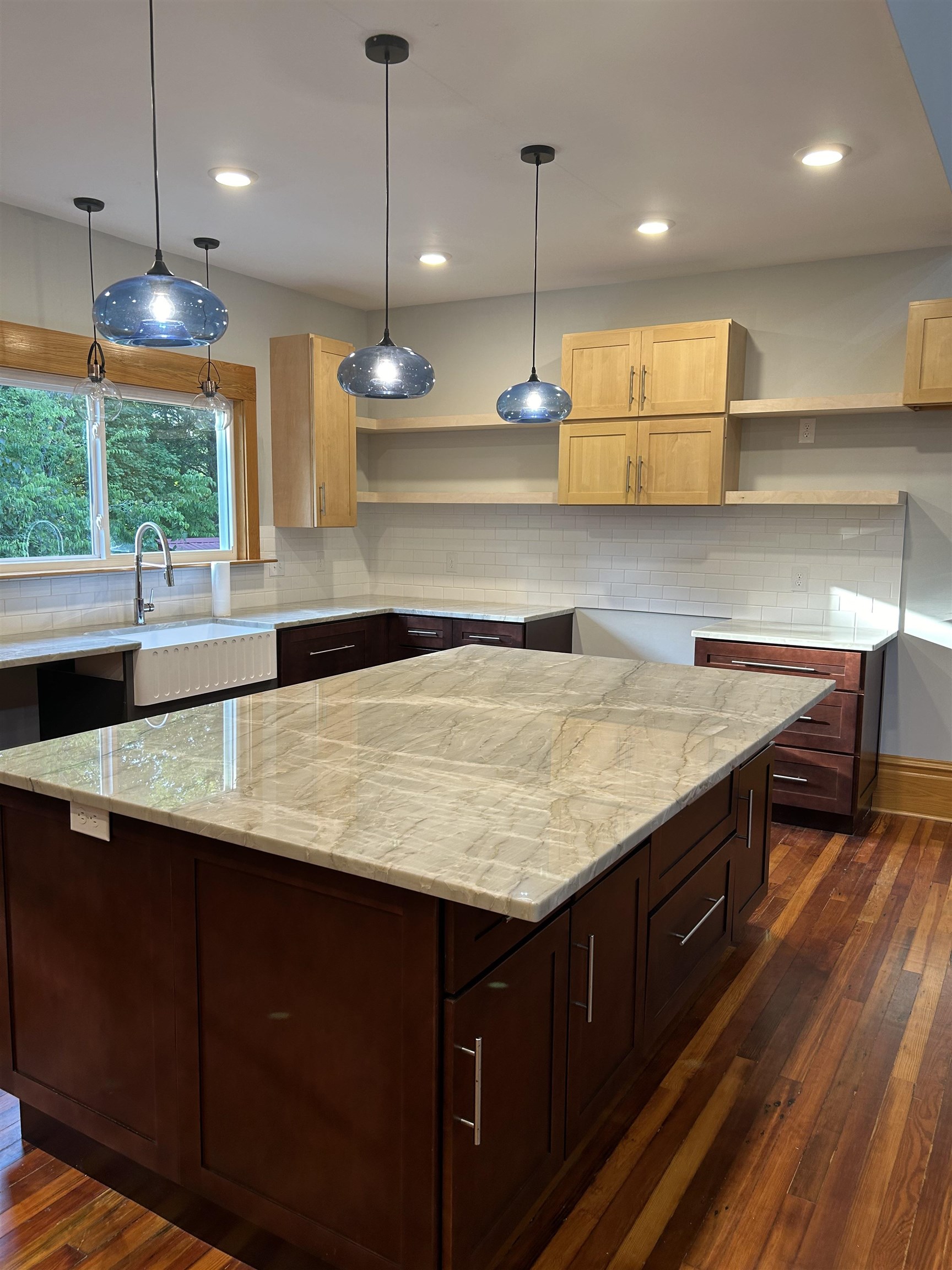 Kitchen with dark wood-type flooring, light stone counters, backsplash, and a kitchen island