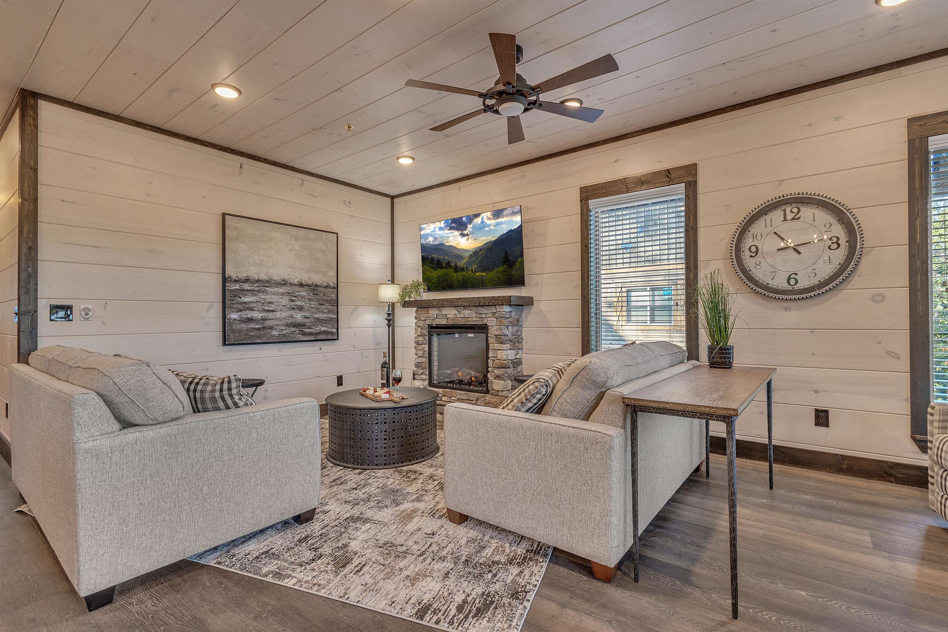 Living room with ceiling fan, a stone fireplace, wood-type flooring, and wooden walls