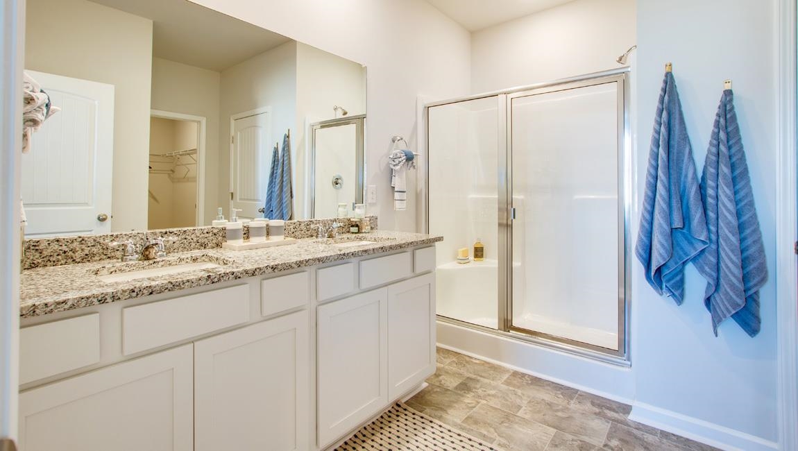 Bathroom with a shower with door, tile flooring, large vanity, and dual sinks