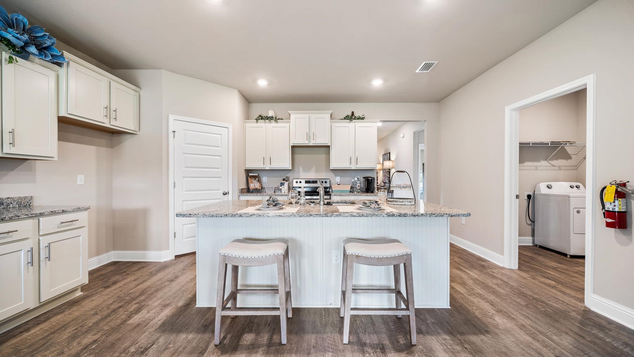 Kitchen with an island with sink, dark hardwood / wood-style flooring, washer / dryer, and light stone countertops
