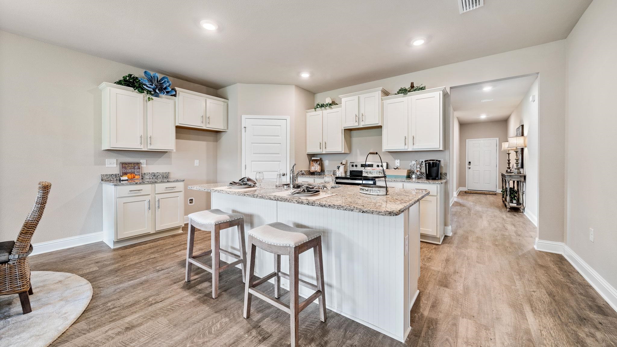 Kitchen with light stone countertops, a center island with sink, white cabinets, hardwood / wood-style floors, and a breakfast bar