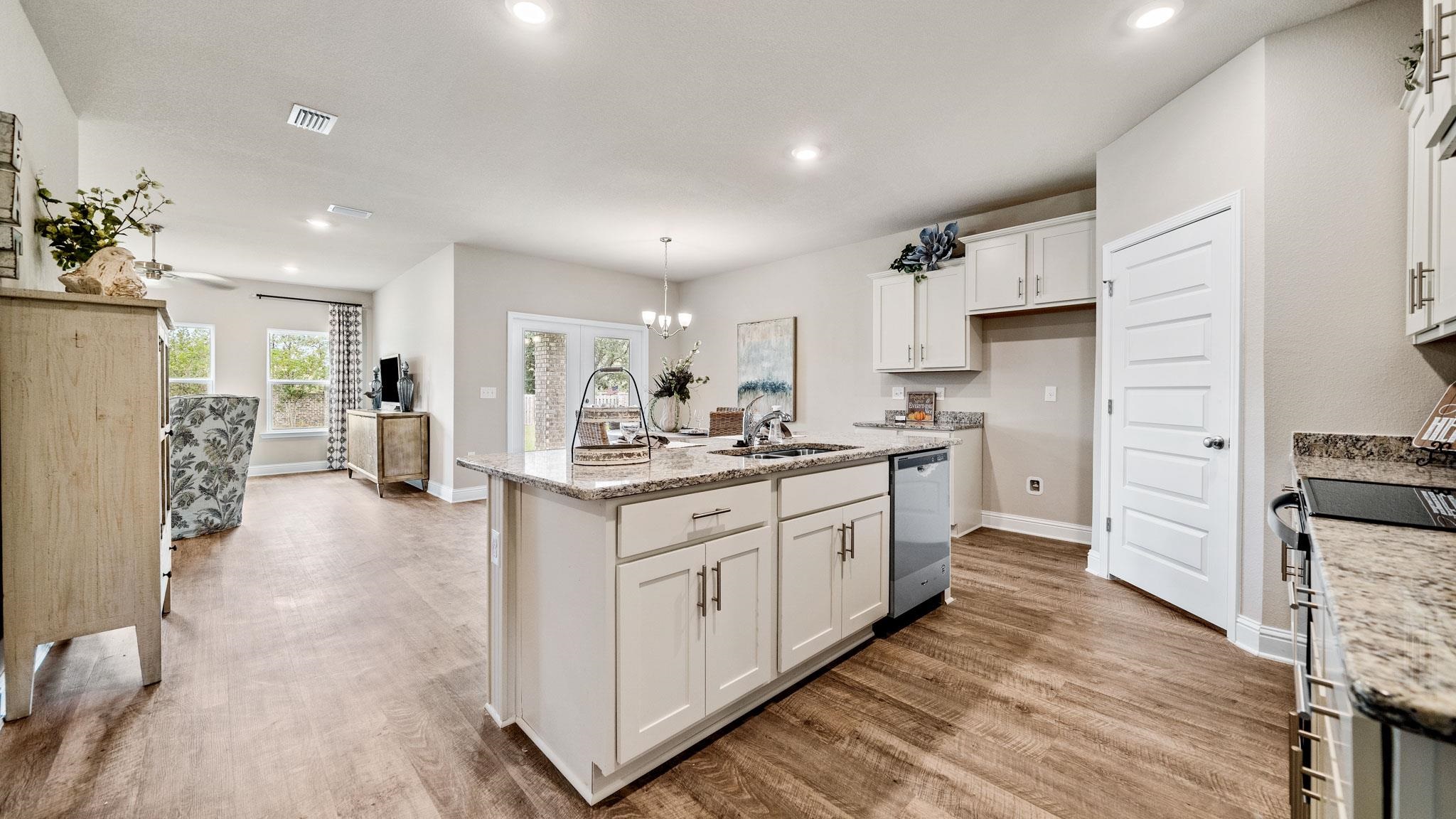 Kitchen featuring hardwood / wood-style flooring, pendant lighting, light stone counters, white cabinets, and a kitchen island with sink