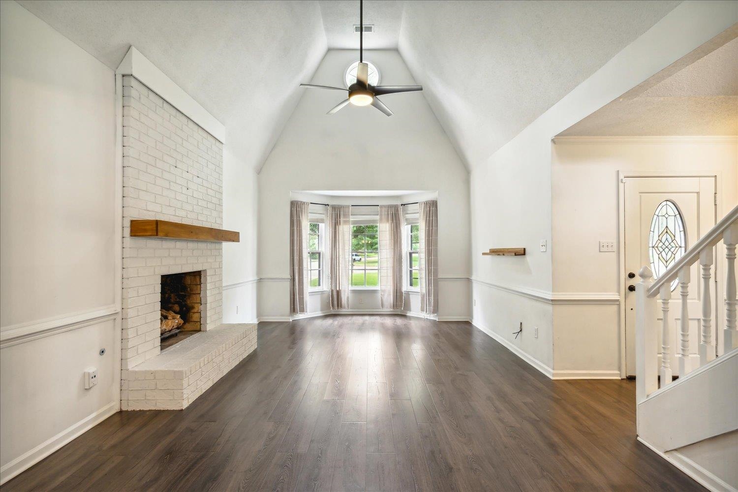 Unfurnished living room with a textured ceiling, dark hardwood / wood-style flooring, a brick fireplace, ceiling fan, and vaulted ceiling