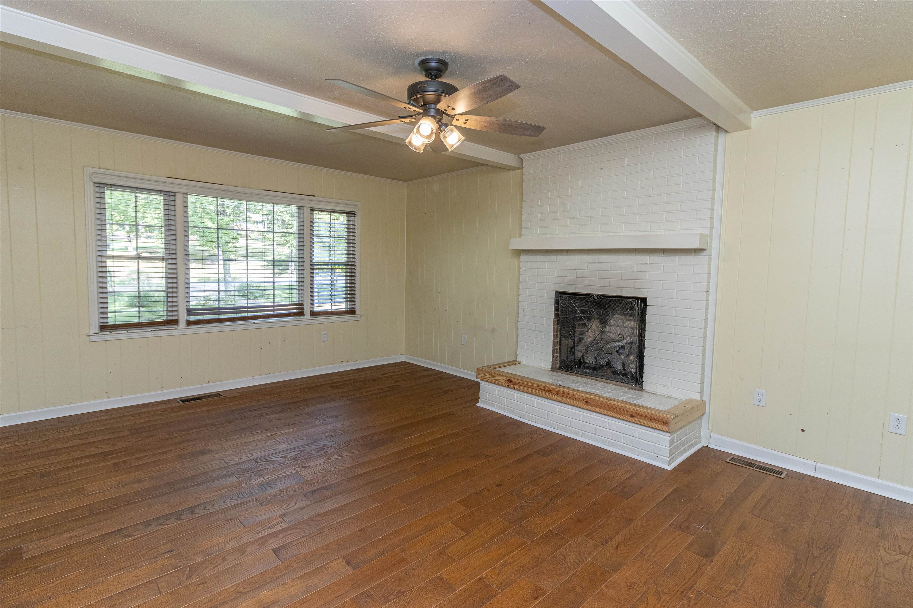 Unfurnished living room featuring a textured ceiling, a brick fireplace, ceiling fan, and dark hardwood / wood-style floors