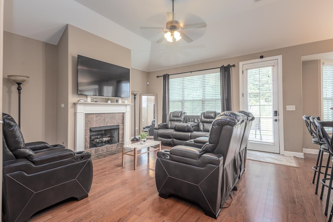 Living room with a tiled fireplace, hardwood / wood-style flooring, and ceiling fan