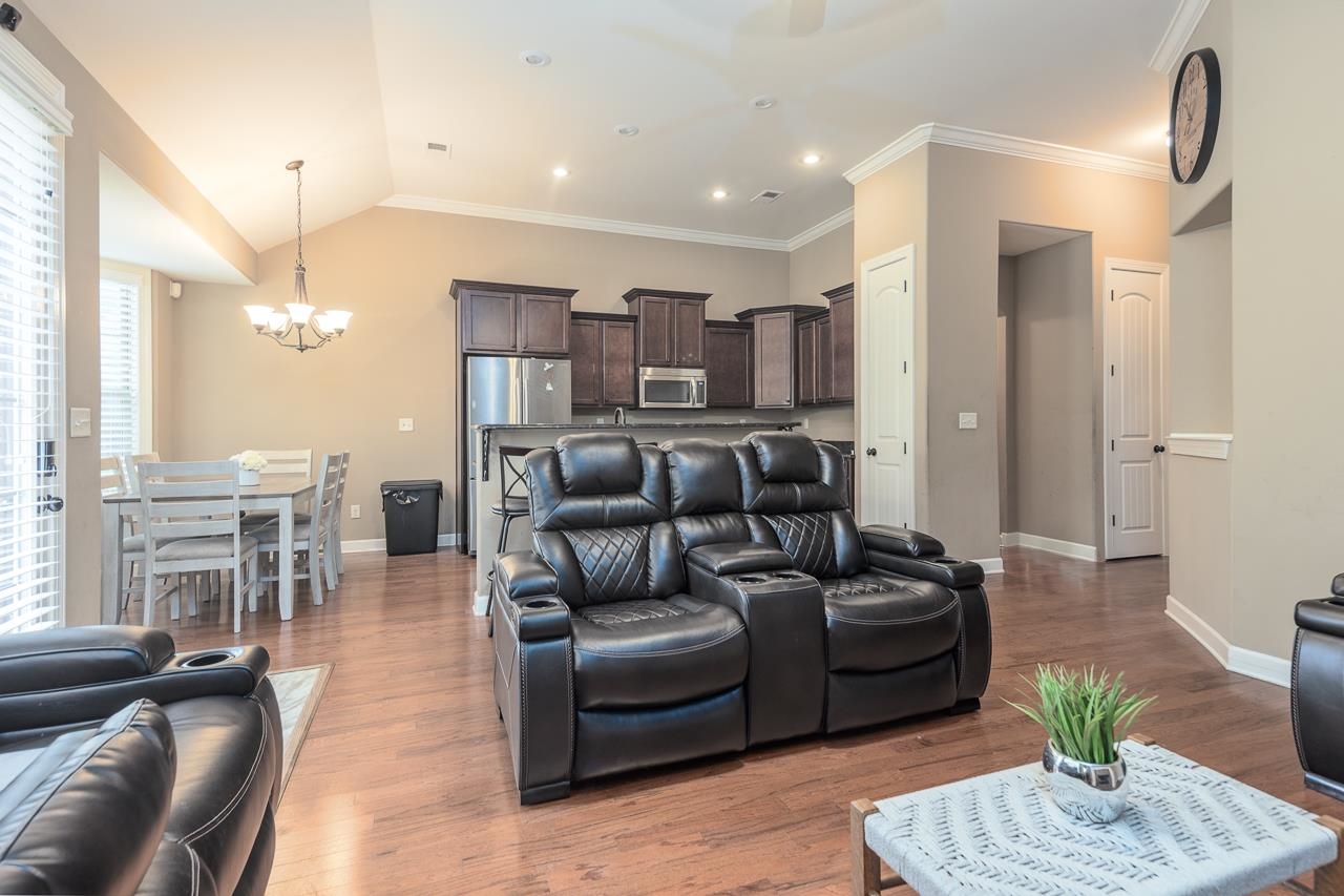 Living room featuring ornamental molding, lofted ceiling, light hardwood / wood-style flooring, and a chandelier