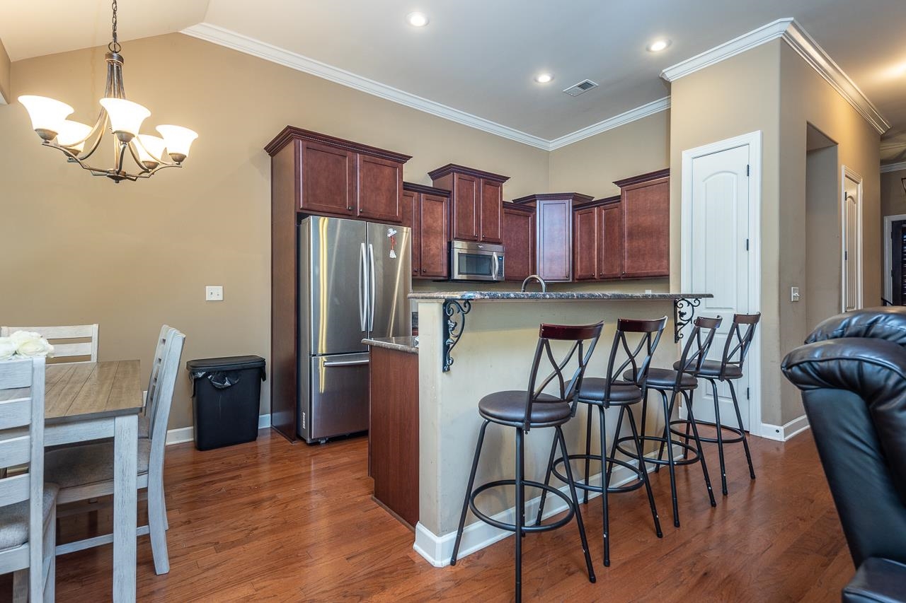 Kitchen featuring dark hardwood / wood-style flooring, a notable chandelier, appliances with stainless steel finishes, a kitchen bar, and ornamental molding