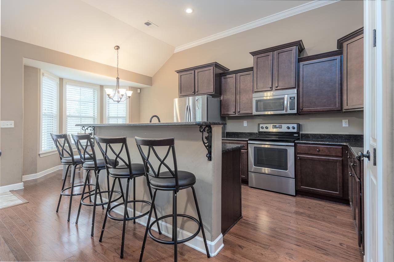 Kitchen with stainless steel appliances, a notable chandelier, wood-type flooring, a breakfast bar area, and a center island with sink