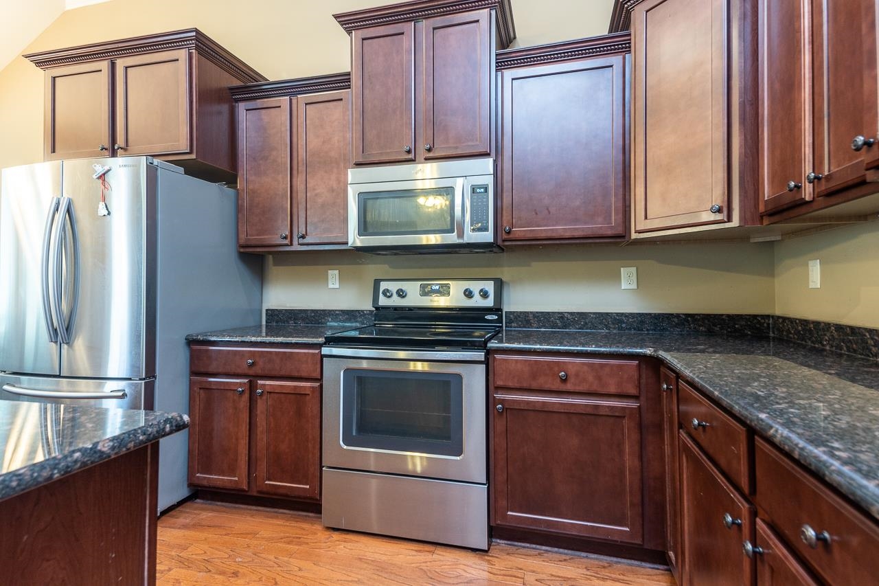 Kitchen with dark stone countertops, stainless steel appliances, and light hardwood / wood-style floors