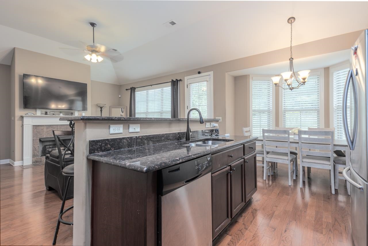Kitchen featuring a tile fireplace, ceiling fan with notable chandelier, stainless steel appliances, sink, and dark stone counters