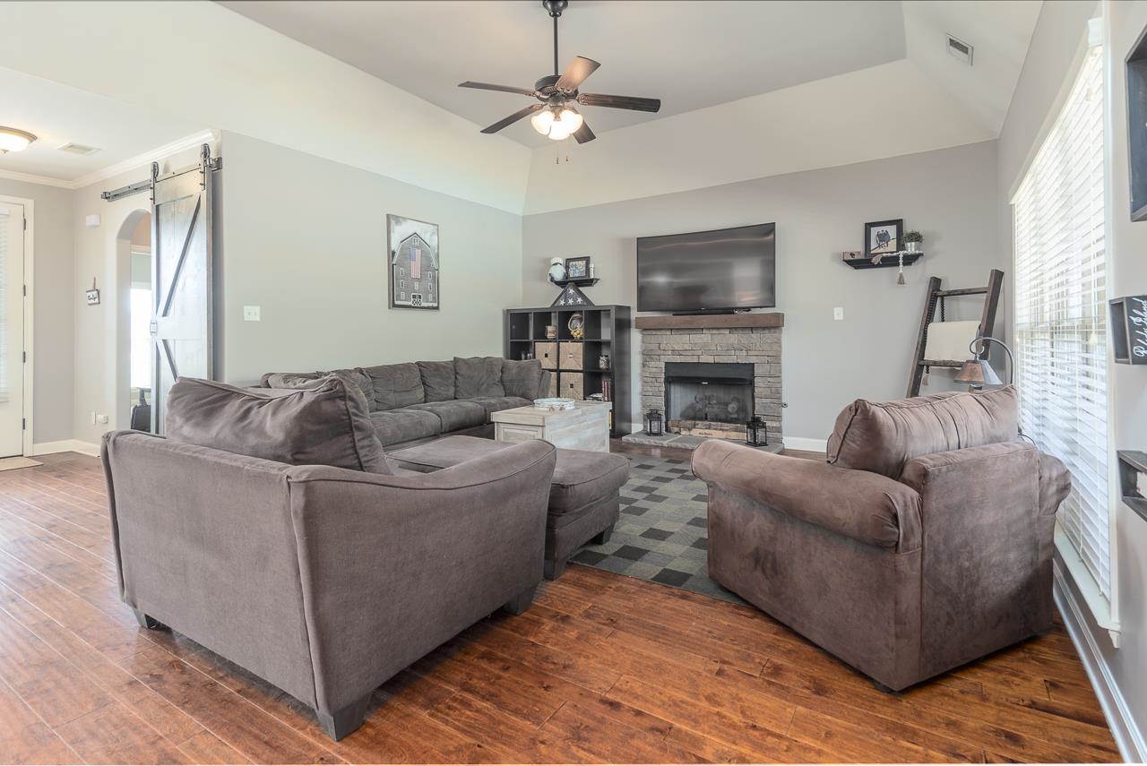 Living room with a gas fireplace, crown molding, dark wood-type flooring, and ceiling fan.  Note the barn door which is fully functional and can be used for added privacy in downstairs bedroom.