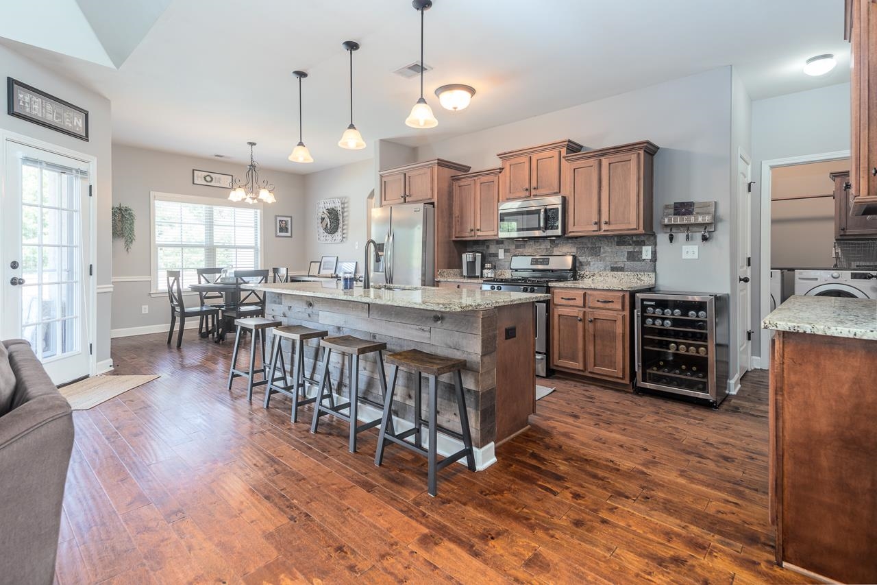 Kitchen featuring decorative light fixtures, dark hardwood /wood-style flooring, a center island with sink, gas range, stainless steel appliances, soft close cabinets