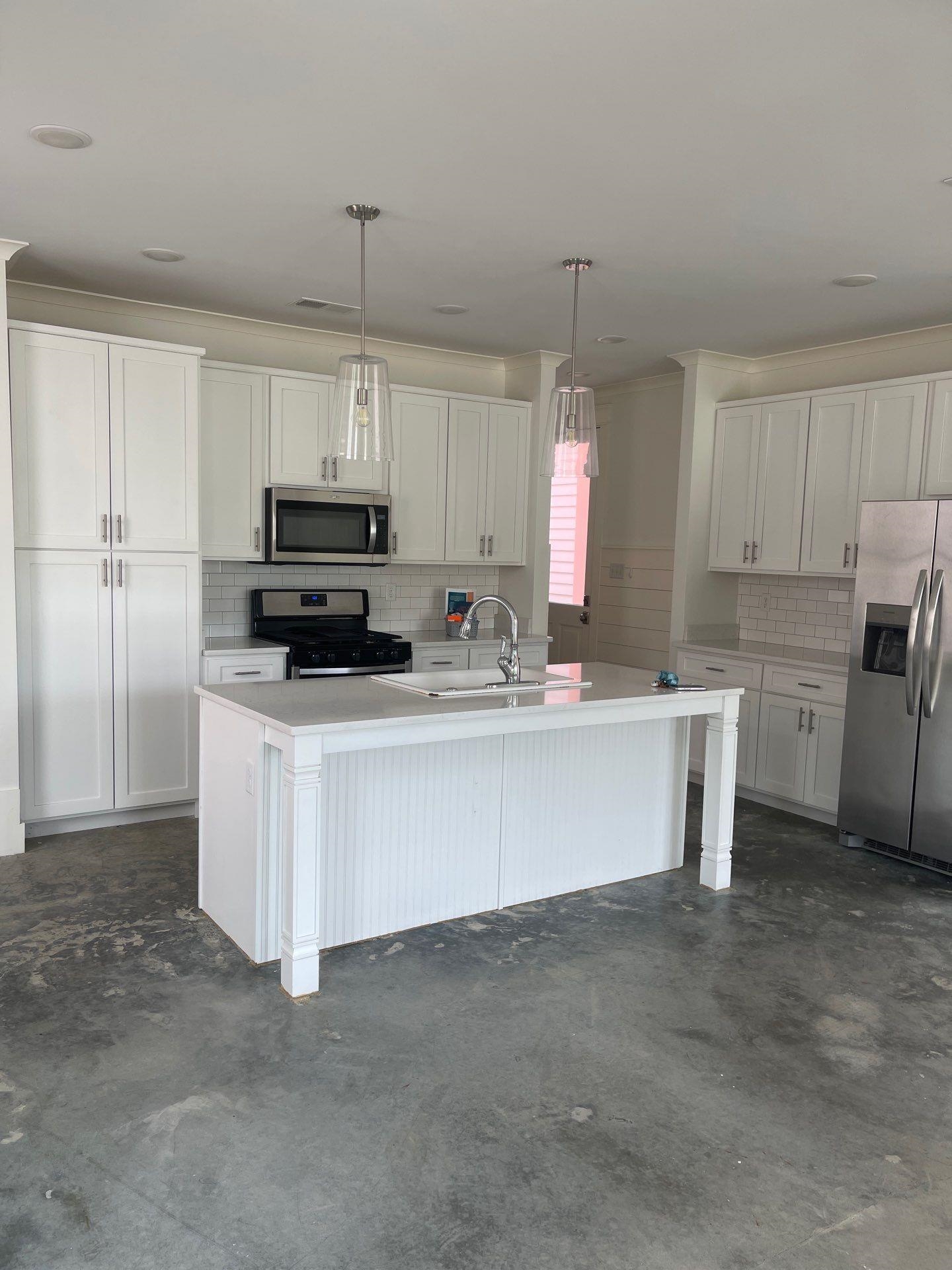 Kitchen with white cabinets, hanging light fixtures, appliances with stainless steel finishes, sink, and a center island with sink