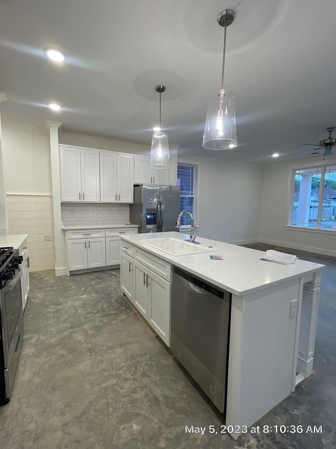Kitchen with a kitchen island with sink, stainless steel appliances, sink, hanging light fixtures, and white cabinets