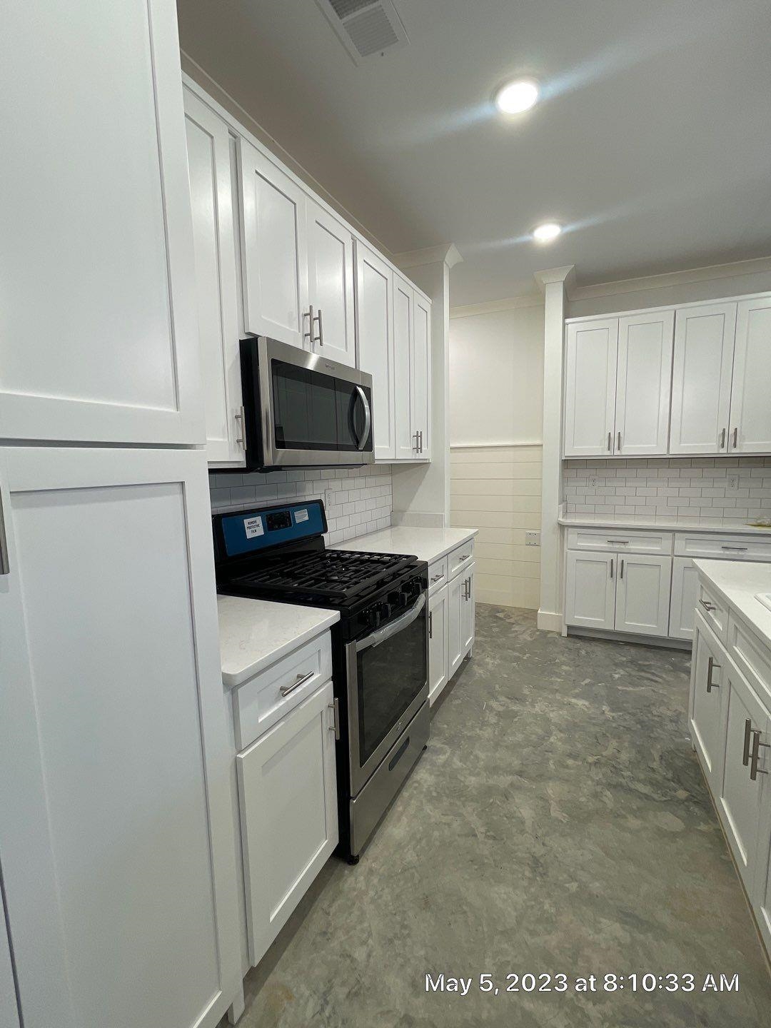 Kitchen with appliances with stainless steel finishes, concrete floors, and white cabinetry