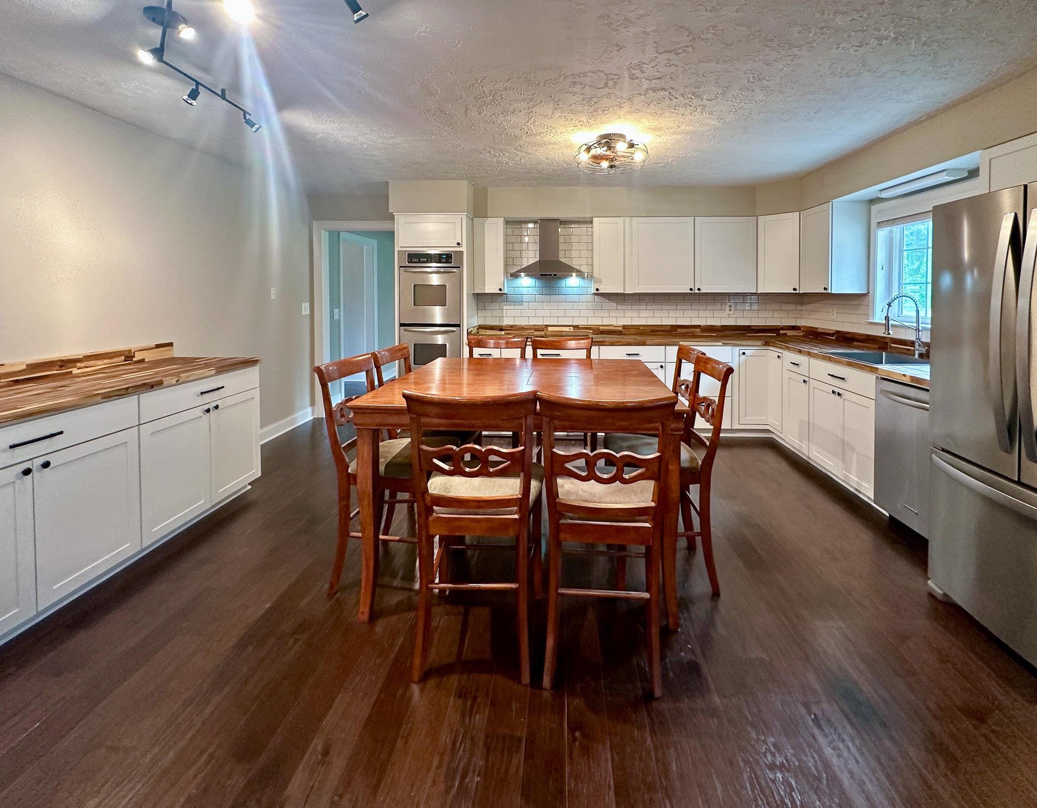 A completely renovated Kitchen featuring stainless steel appliances, butcher block countertops, dark hardwood / wood-style floors, wall chimney exhaust hood, and a textured ceiling