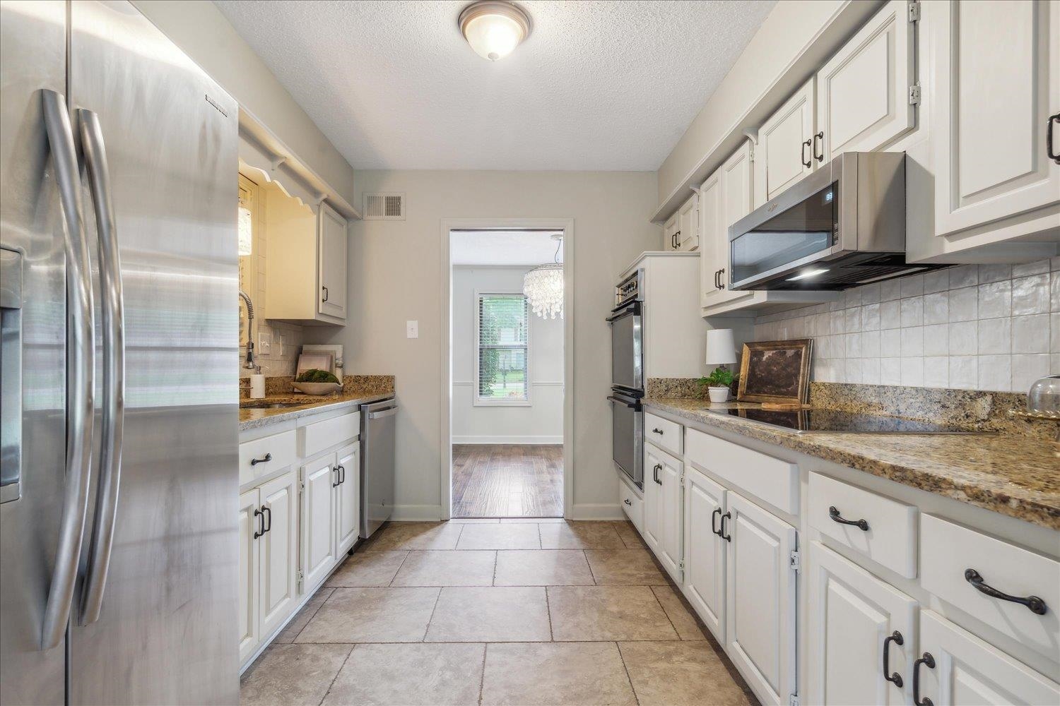 Kitchen featuring light tile flooring, light stone counters, backsplash, white cabinetry, and appliances with stainless steel finishes