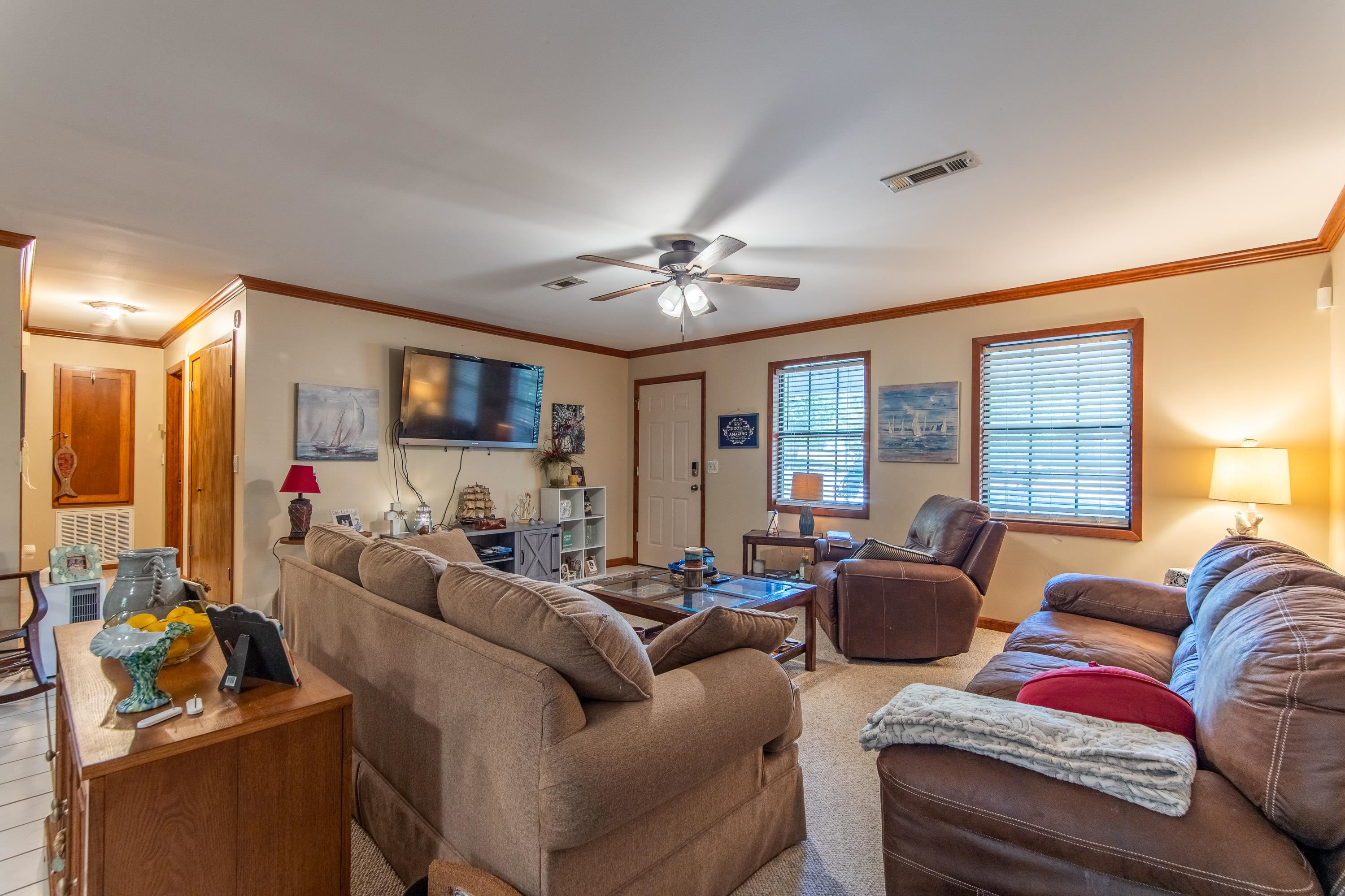 Living room with carpet flooring, ceiling fan, and ornamental molding