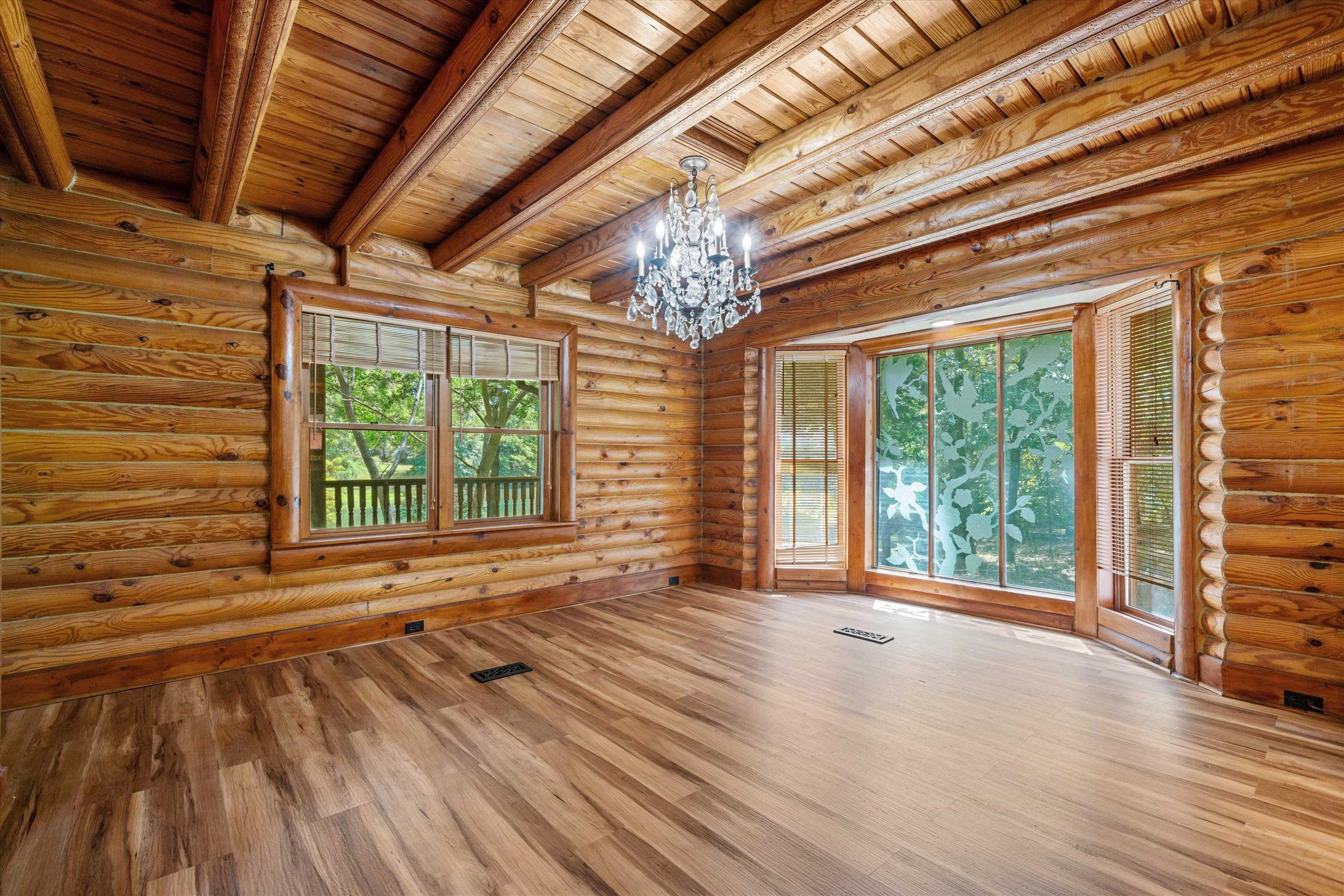 Spare room with an inviting chandelier, wood ceiling, beamed ceiling, wood-type flooring, and rustic walls