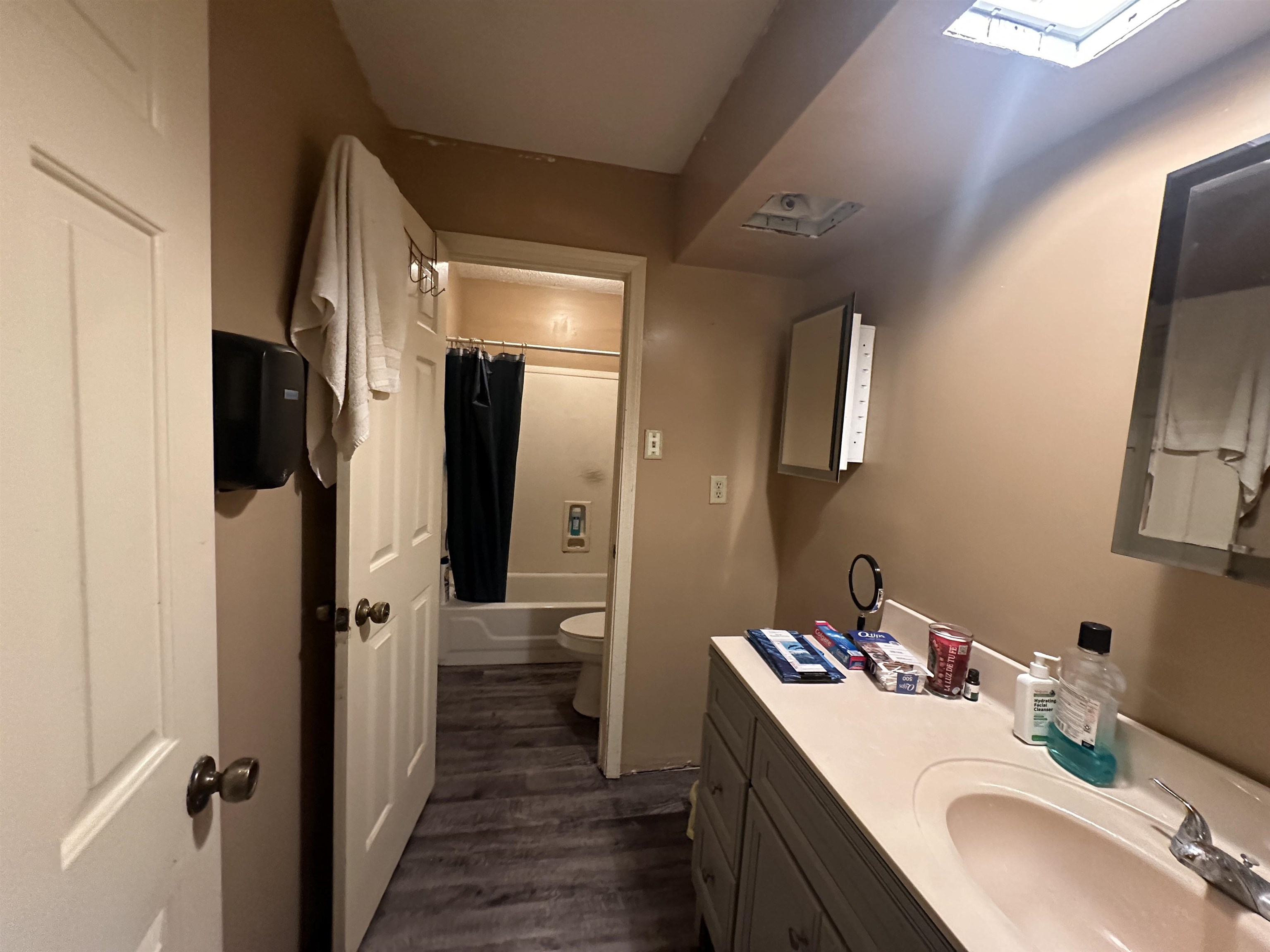 Full bathroom featuring toilet, vanity, a skylight, wood-type flooring, and shower / bath combination with curtain