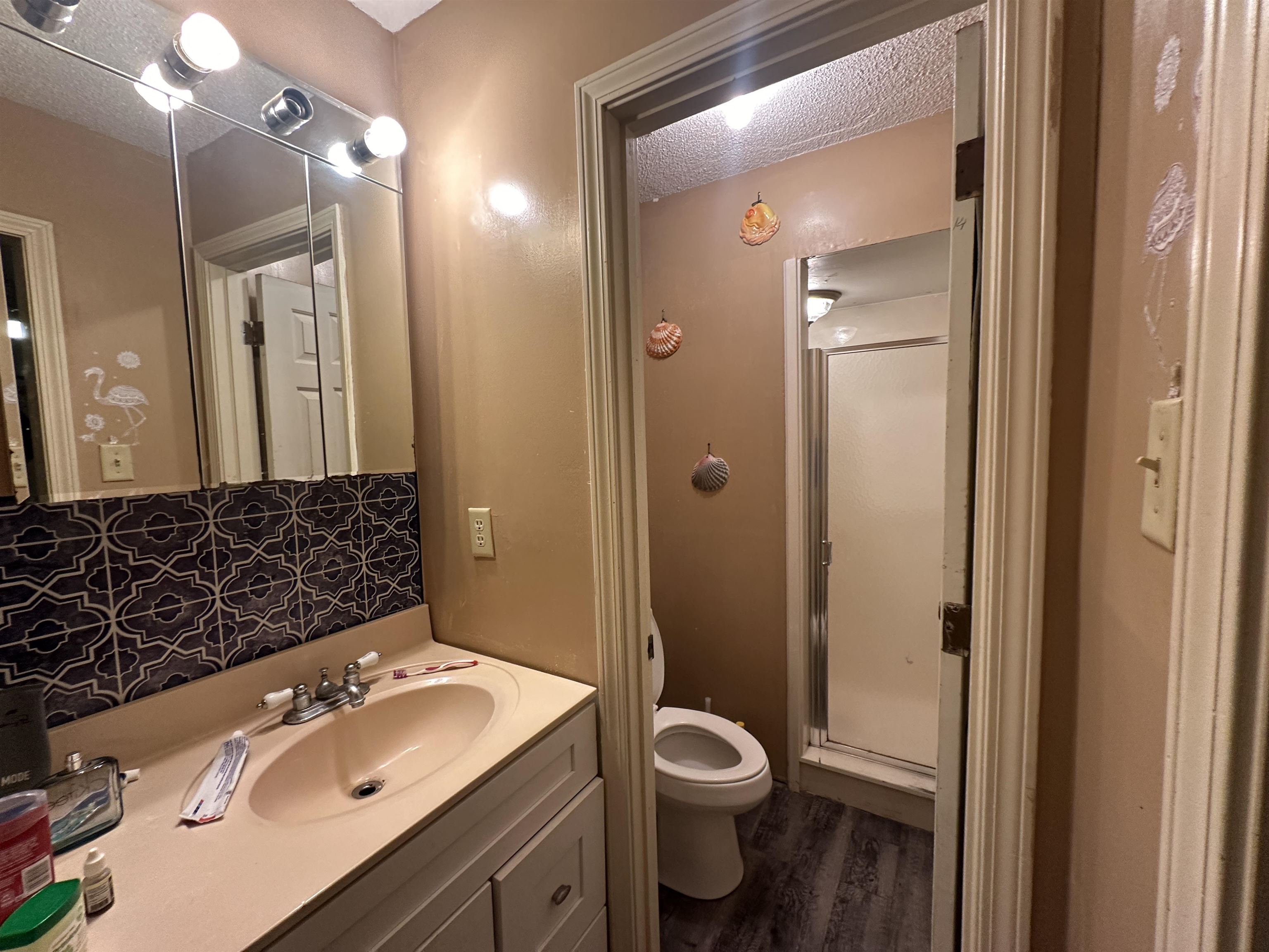 Bathroom featuring a shower with door, vanity, a textured ceiling, hardwood / wood-style floors, and toilet