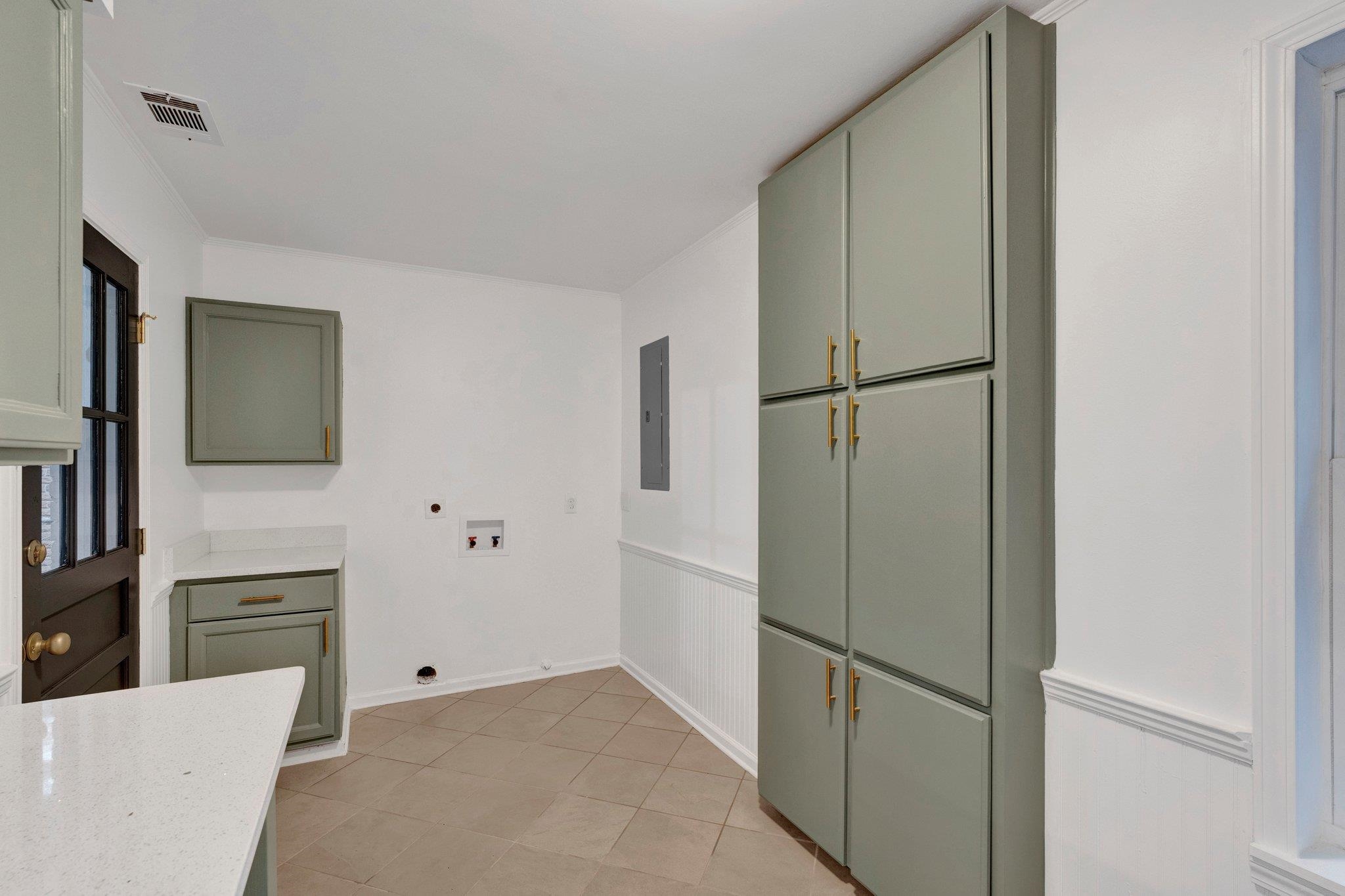 Kitchen with light tile patterned floors, electric panel, light stone counters, and green cabinets