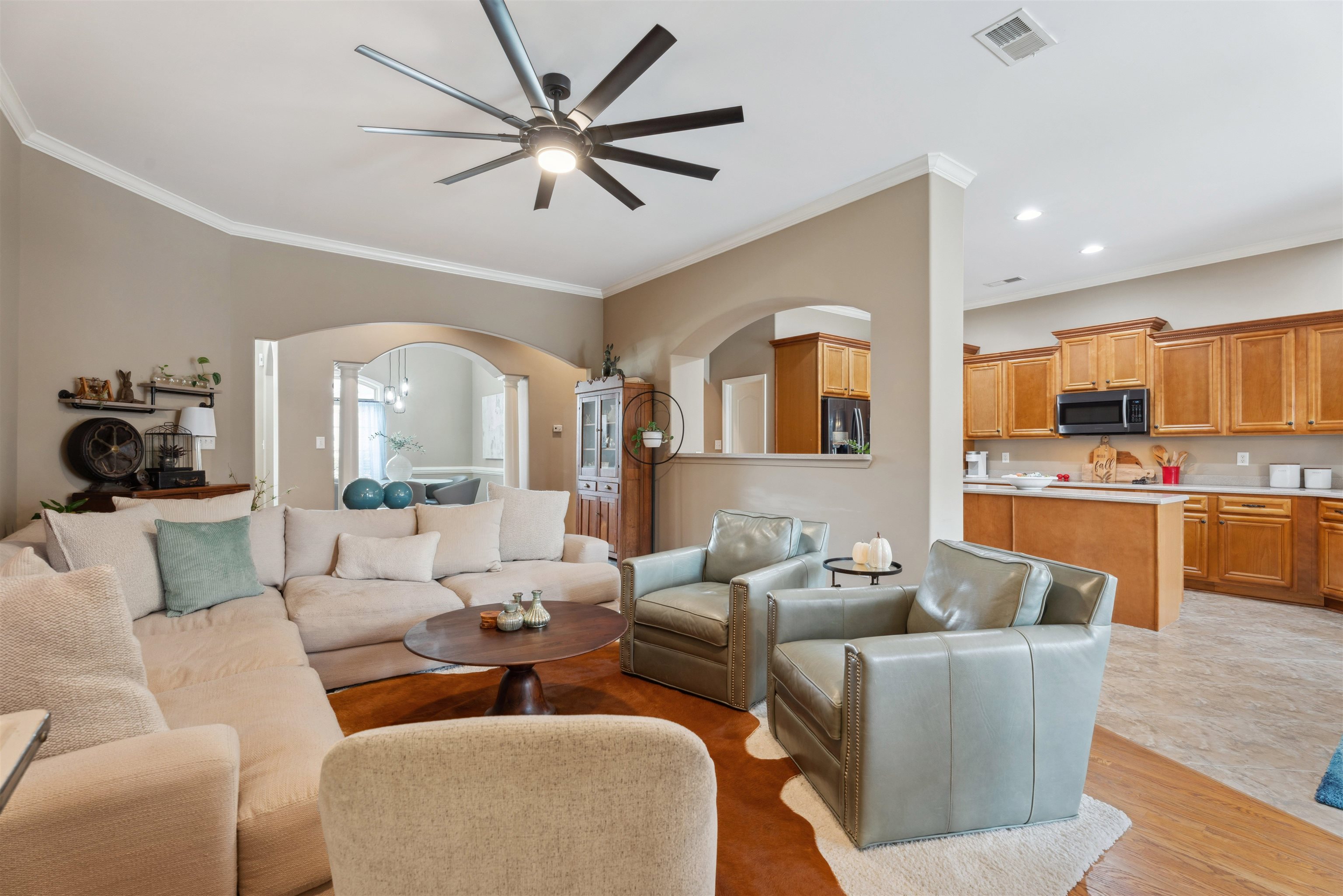 Living room featuring ceiling fan with notable chandelier, ornamental molding, and light hardwood / wood-style flooring