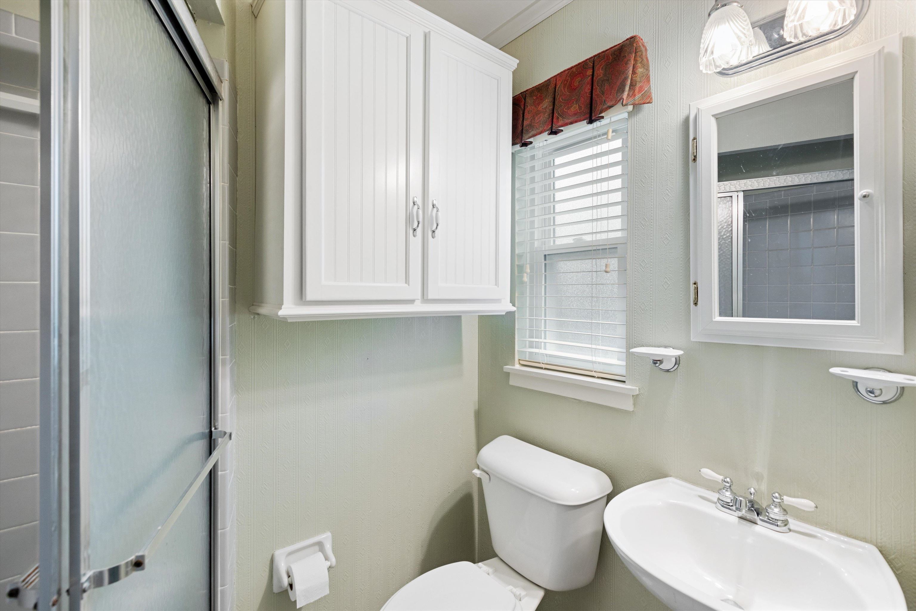 Bathroom featuring toilet, ornamental molding, sink, and a shower with shower door