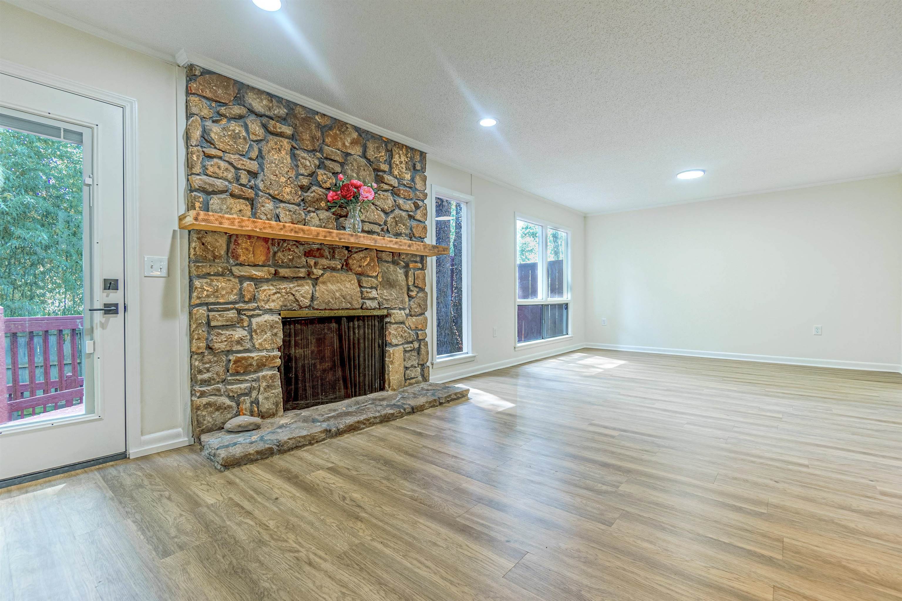 Unfurnished living room with a textured ceiling, ornamental molding, a stone fireplace, and hardwood / wood-style flooring