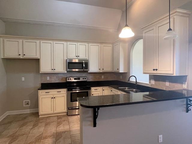 Kitchen featuring ornamental molding, appliances with stainless steel finishes, kitchen peninsula, and hanging light fixtures