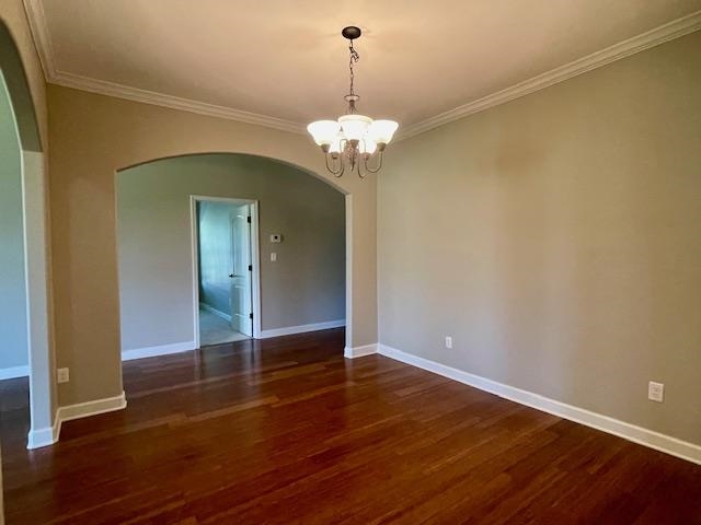 Spare room with crown molding, dark wood-type flooring, and a chandelier