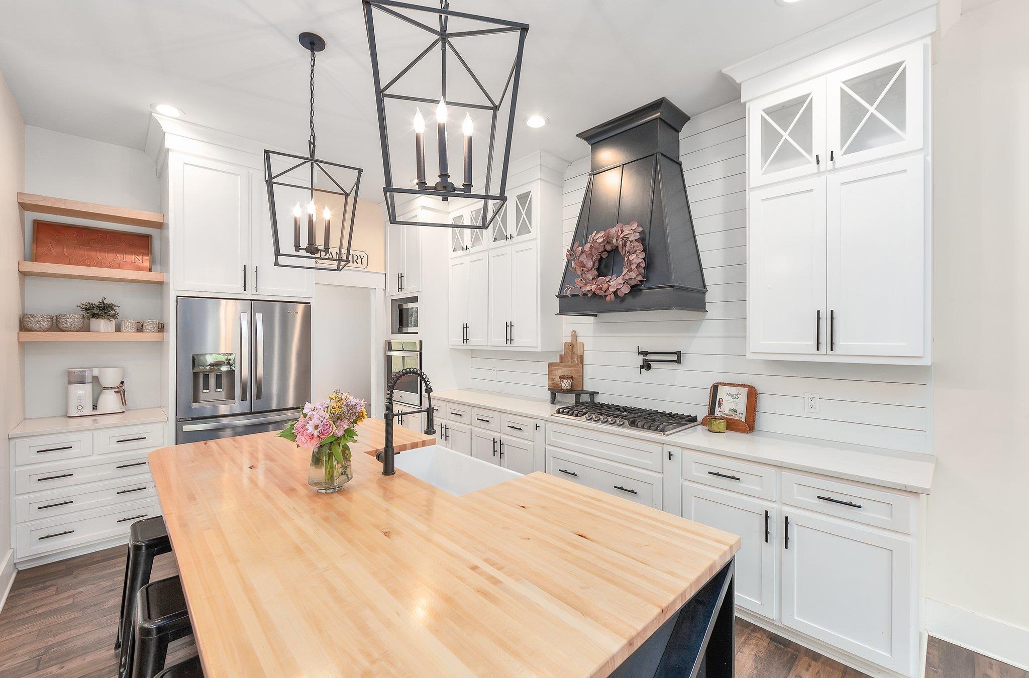 Kitchen with white cabinetry, a chandelier, stainless steel appliances, dark wood-type flooring, and custom range hood