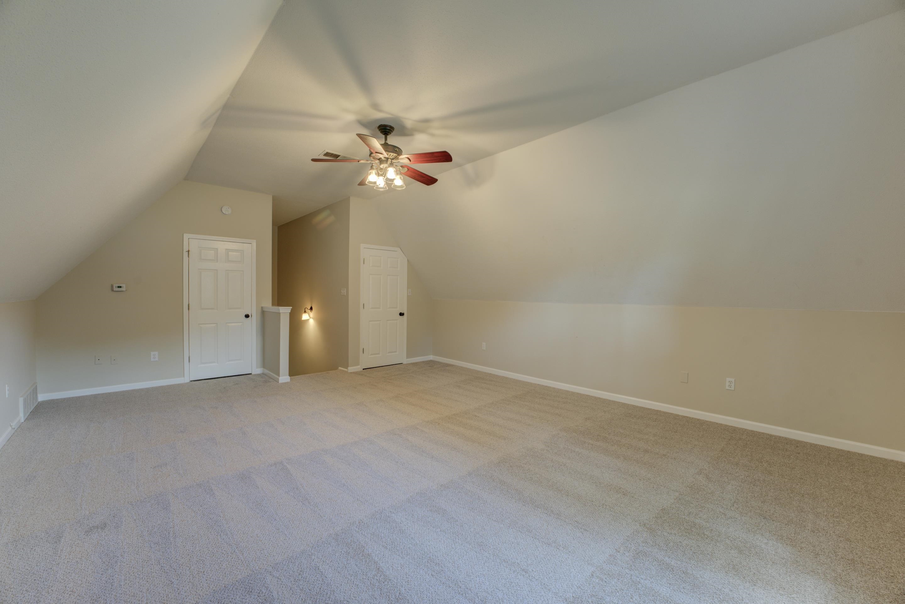 Bonus room with lofted ceiling, light colored carpet, and ceiling fan