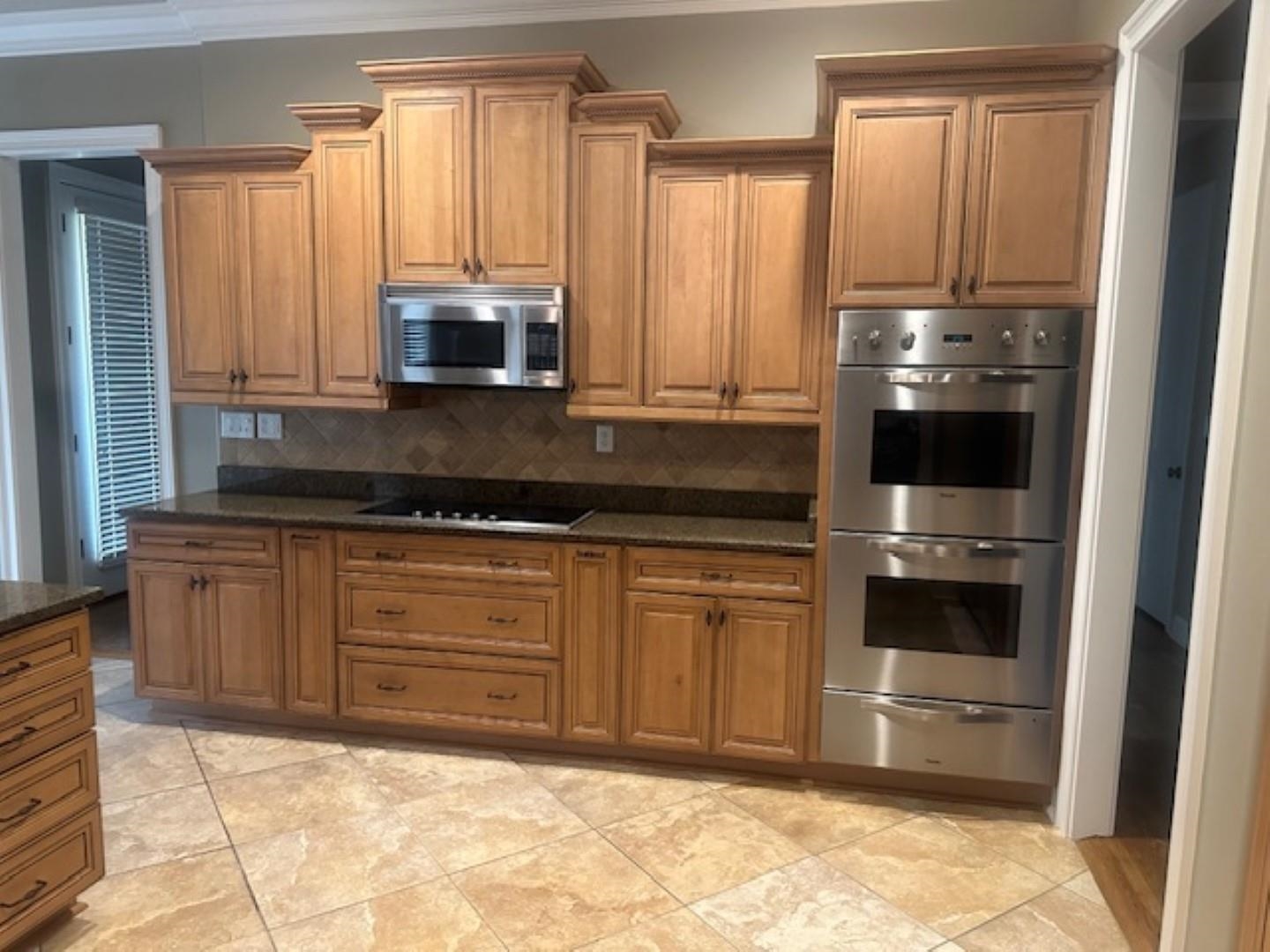 Kitchen with decorative backsplash, ornamental molding, appliances with stainless steel finishes, light tile patterned floors, and dark stone countertops