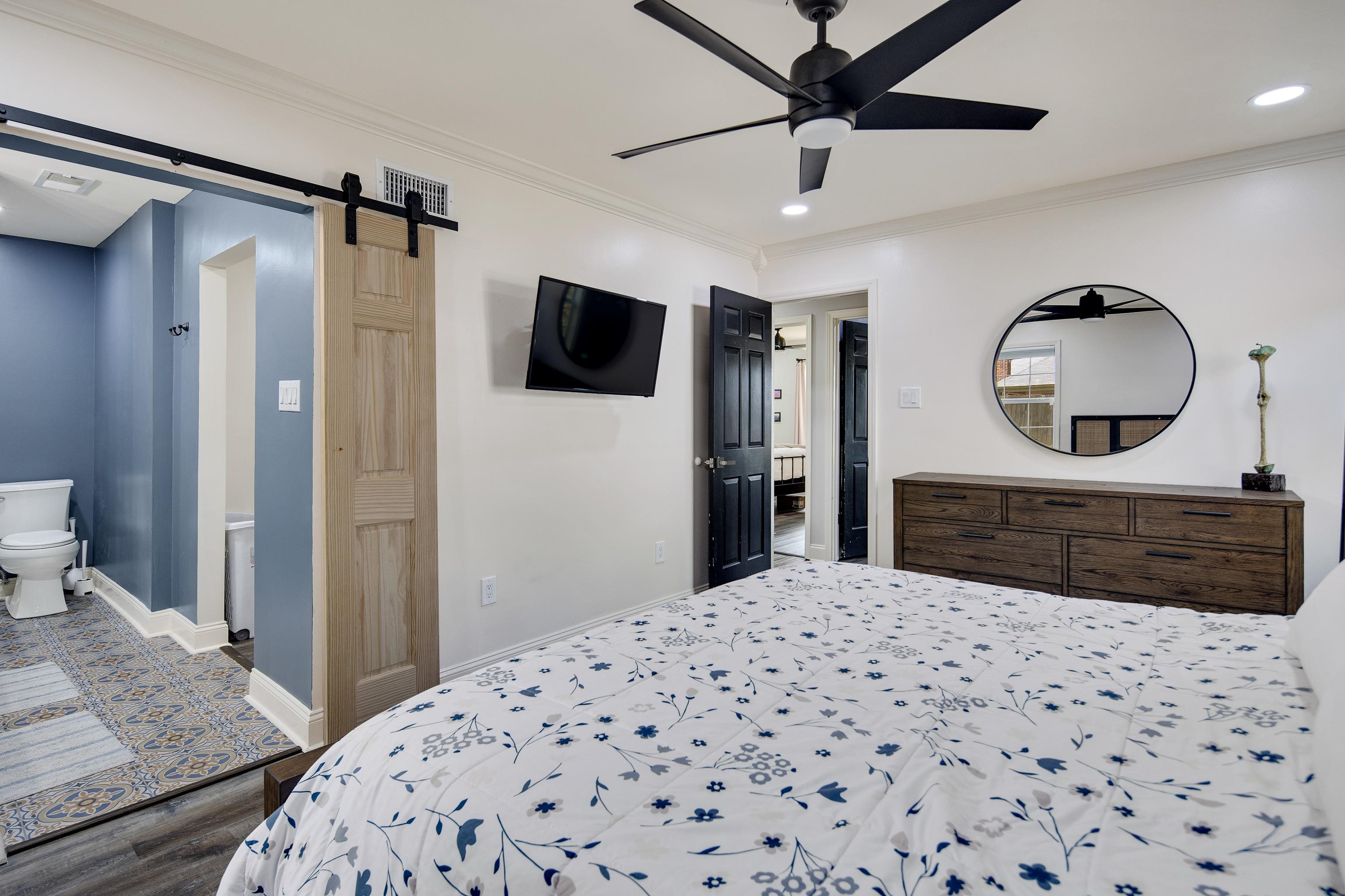 Bedroom with ensuite bathroom, crown molding, a barn door, wood-type flooring, and ceiling fan