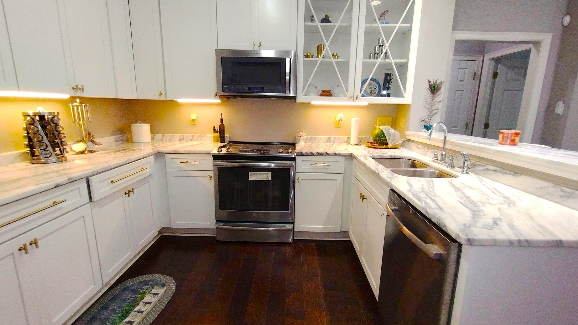 Kitchen featuring appliances with stainless steel finishes, dark wood-type flooring, kitchen peninsula, sink, and light stone counters