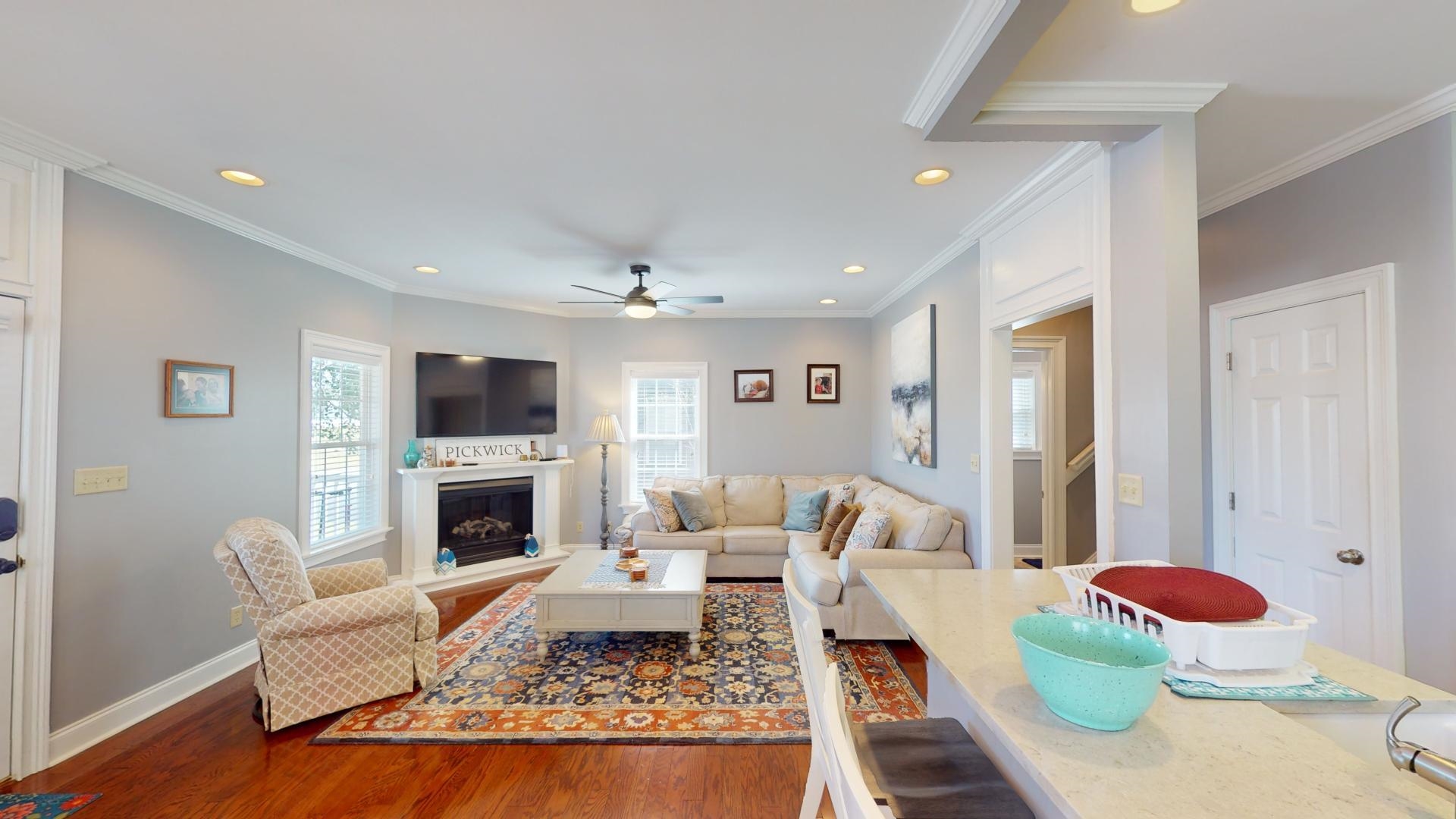 Living room featuring dark wood-type flooring, ceiling fan, a wealth of natural light, and crown molding