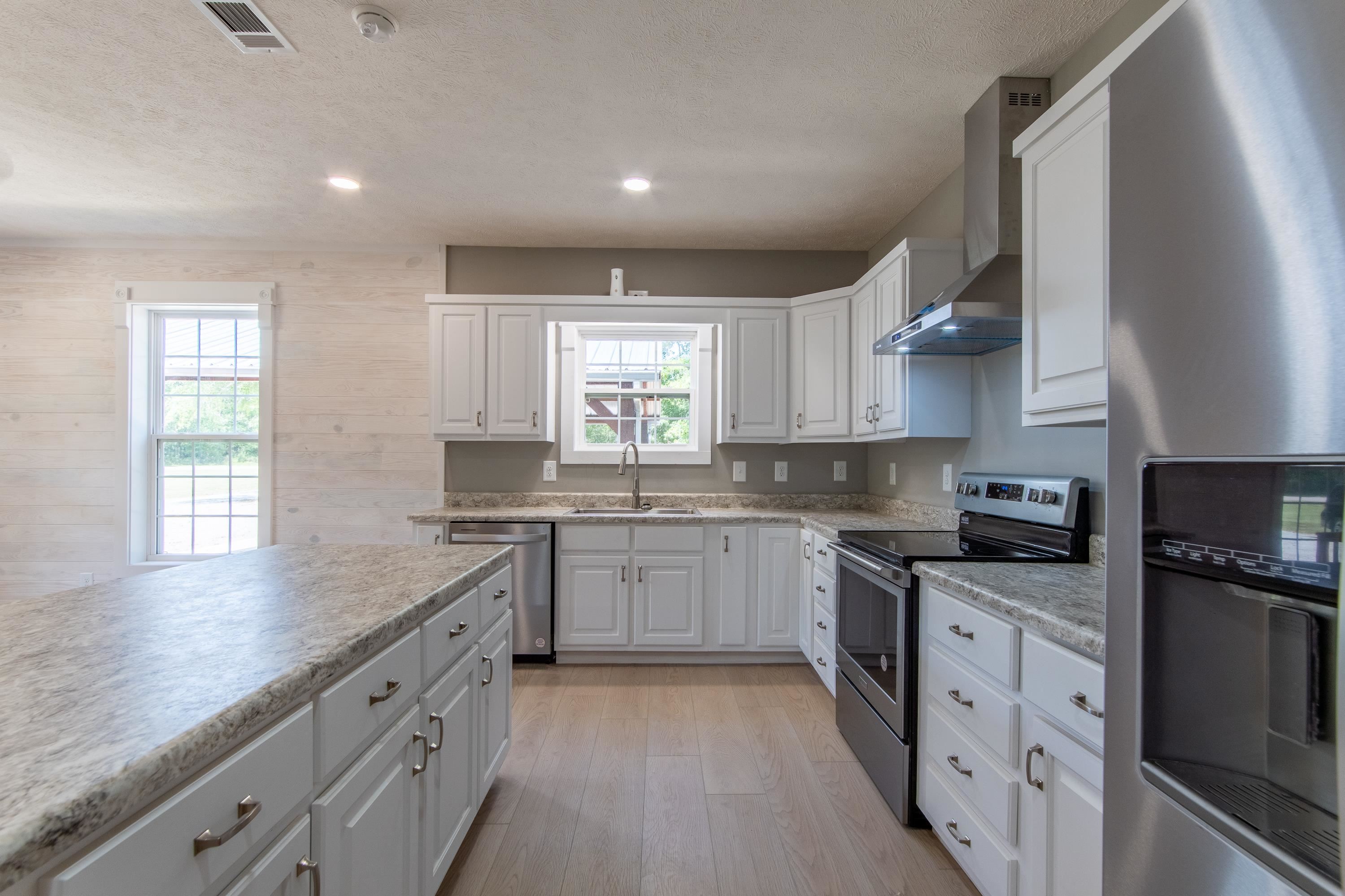 Kitchen featuring wood walls, wall chimney range hood, appliances with stainless steel finishes, white cabinets, and light hardwood / wood-style floors