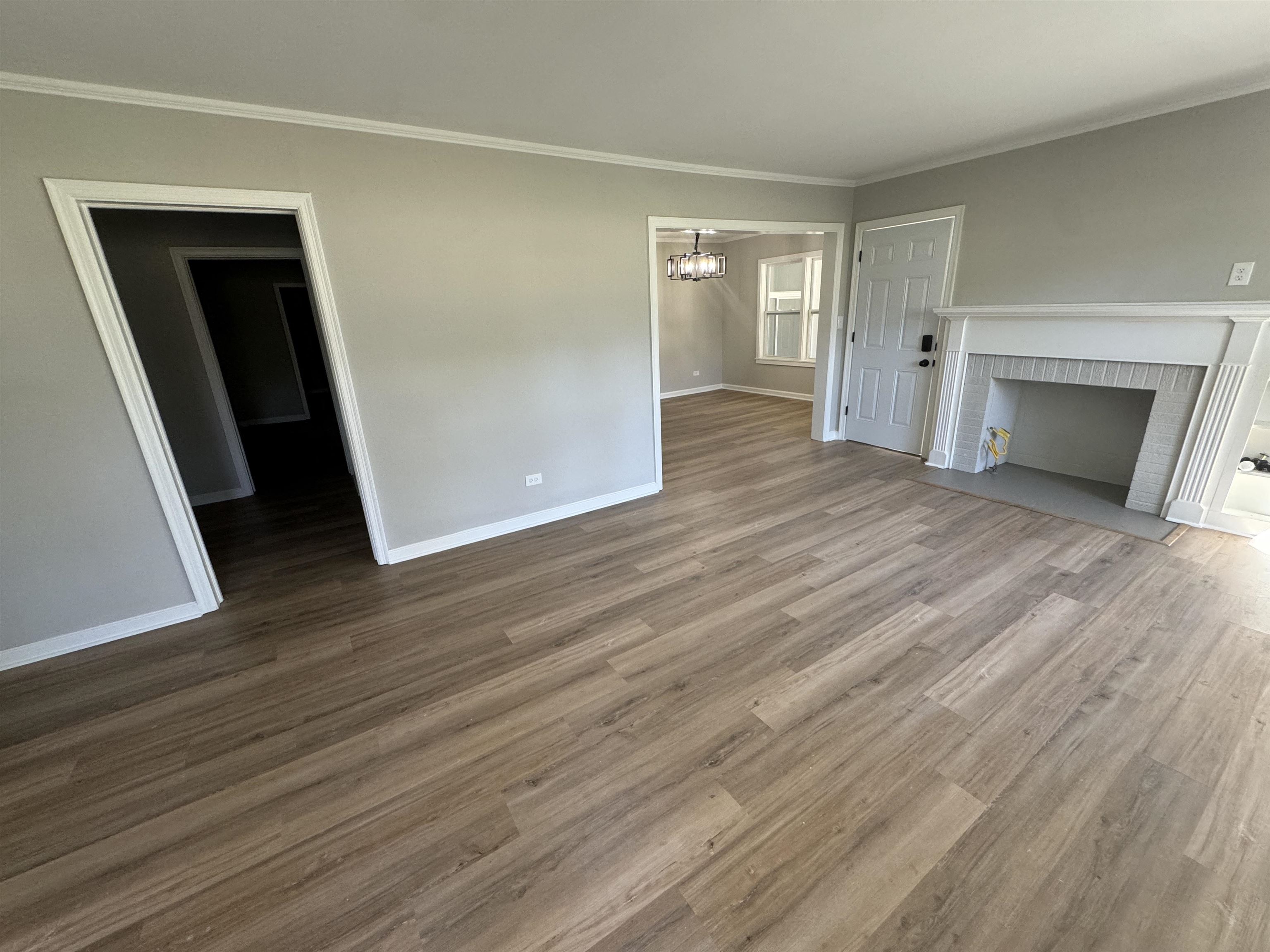 Unfurnished living room with wood-type flooring, a fireplace, an inviting chandelier, and crown molding