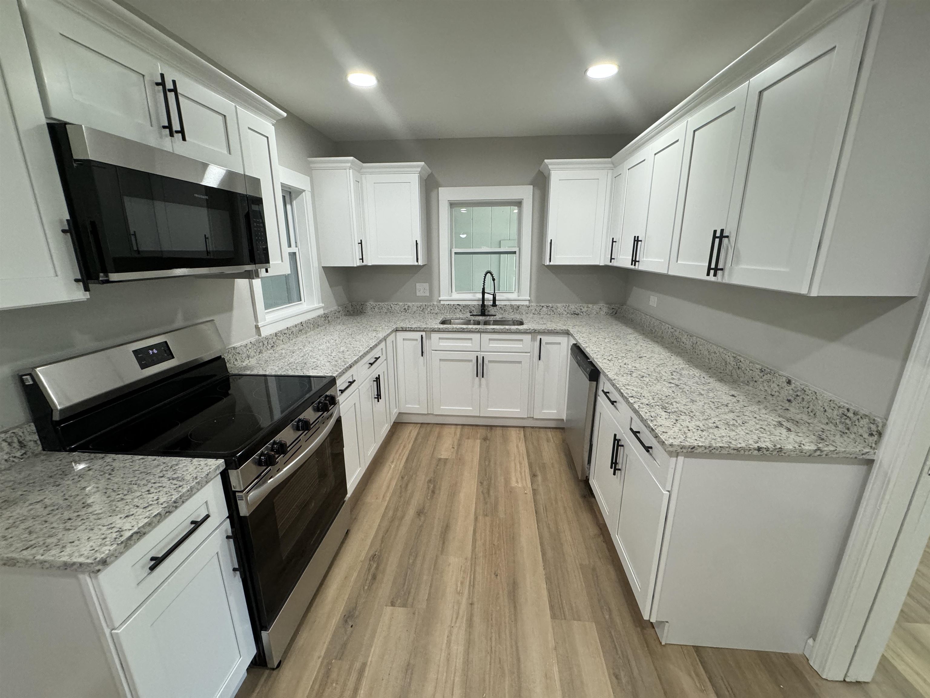 Kitchen featuring light stone countertops, light hardwood / wood-style floors, stainless steel appliances, sink, and white cabinets