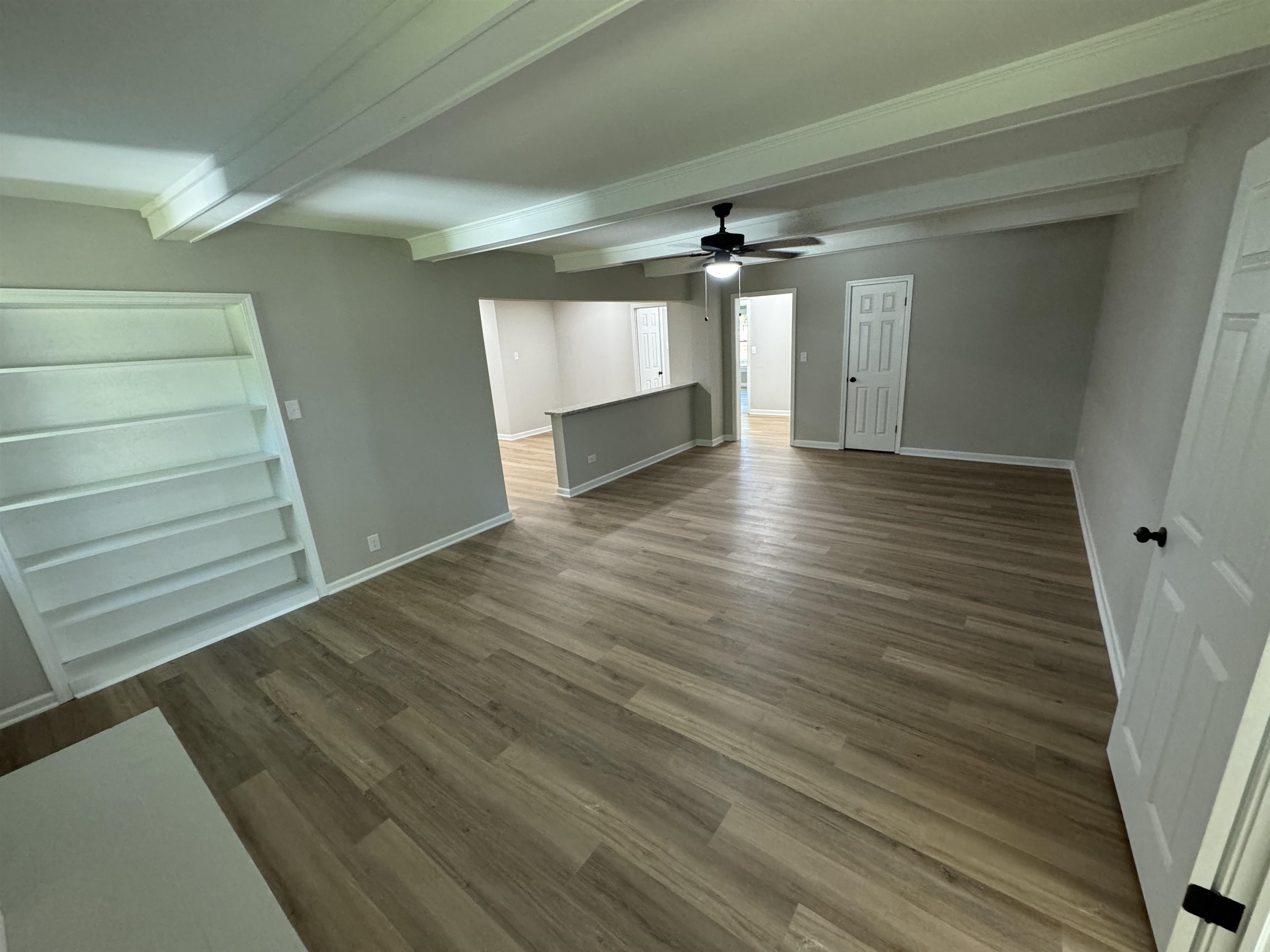 Unfurnished living room featuring hardwood / wood-style floors, ceiling fan, and beamed ceiling