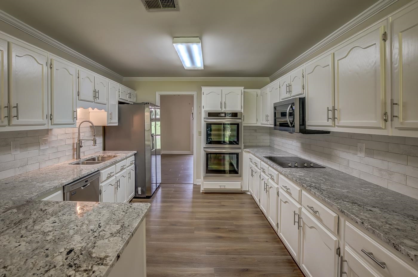 Kitchen featuring crown molding, sink, light stone countertops, appliances with stainless steel finishes, and hardwood / wood-style flooring