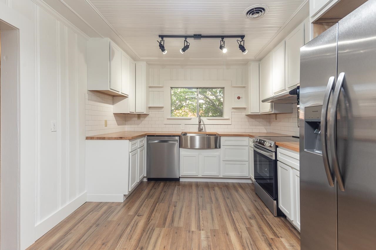 Kitchen with wood-type flooring, stainless steel appliances, butcher block countertops, and white cabinets