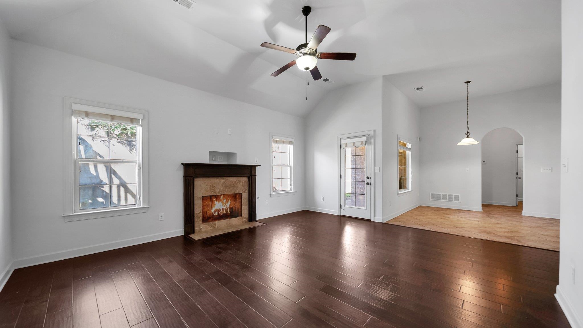 Unfurnished living room featuring a high end fireplace, dark wood-type flooring, high vaulted ceiling, and ceiling fan