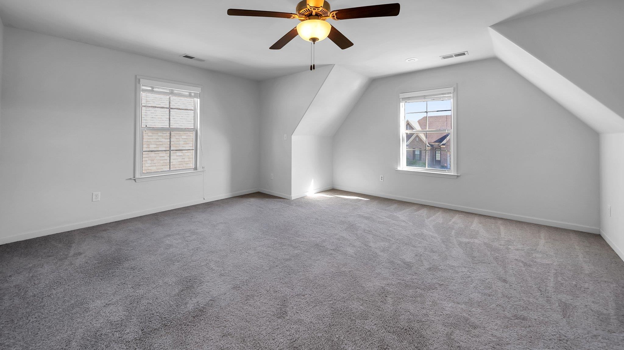 Bonus room with lofted ceiling, plenty of natural light, ceiling fan, and carpet flooring