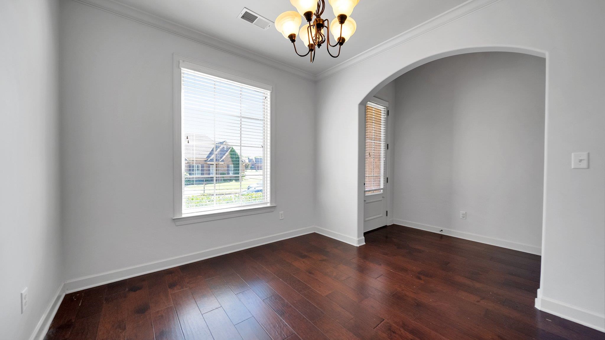 Empty room featuring dark hardwood / wood-style floors, an inviting chandelier, and crown molding