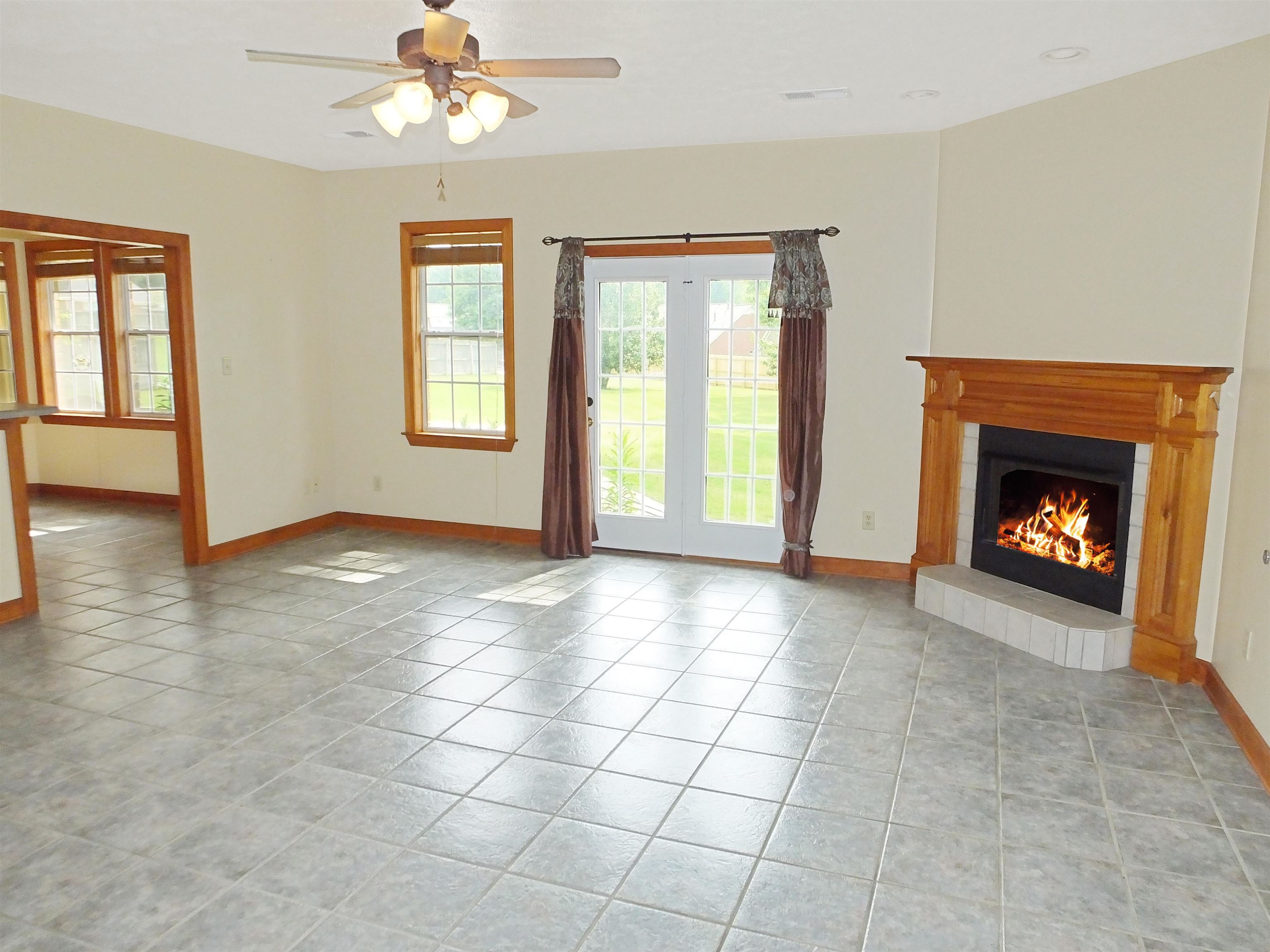 Unfurnished living room with ceiling fan, light tile patterned floors, and a tiled fireplace